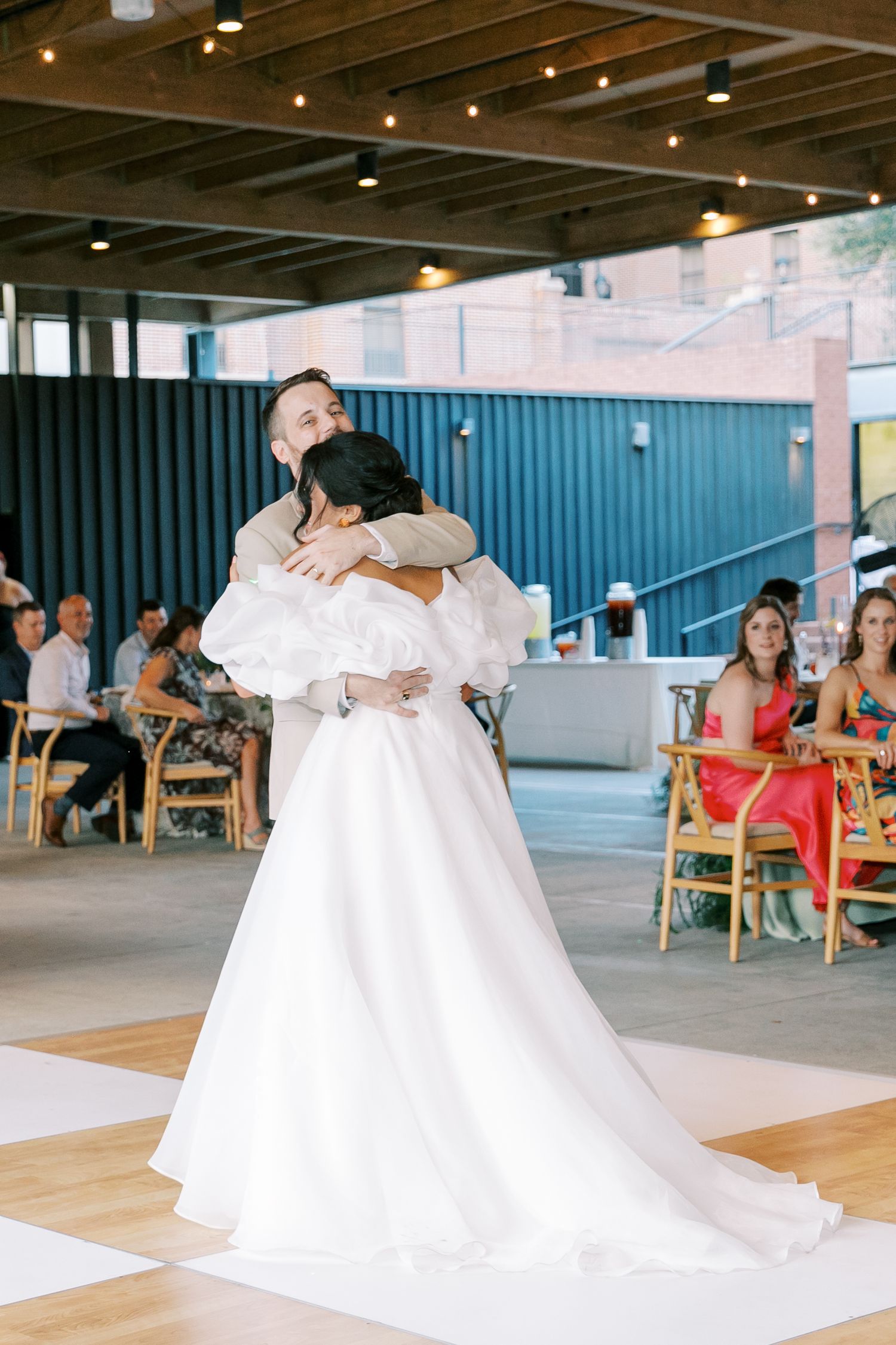 A tender embrace during a first dance at an indoor wedding reception with guests watching.