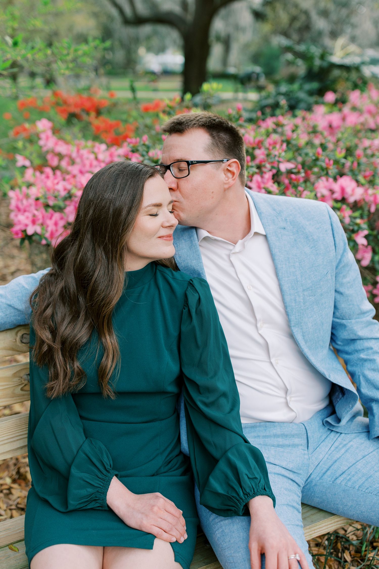 A romantic couple sharing an intimate moment among blooming pink flowers in a garden setting.