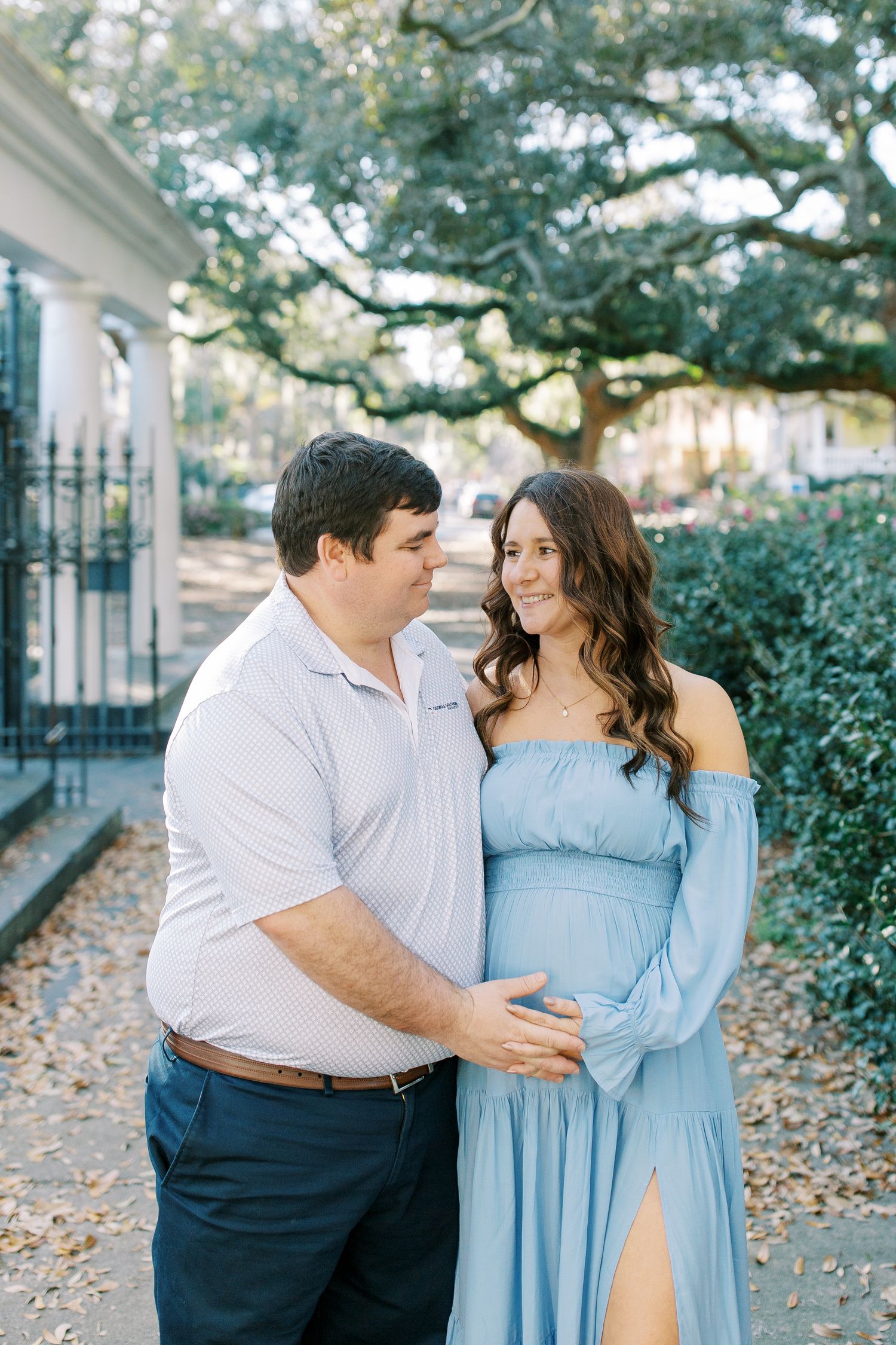 A tender moment between a couple in coordinating outfits against a backdrop of oak trees.