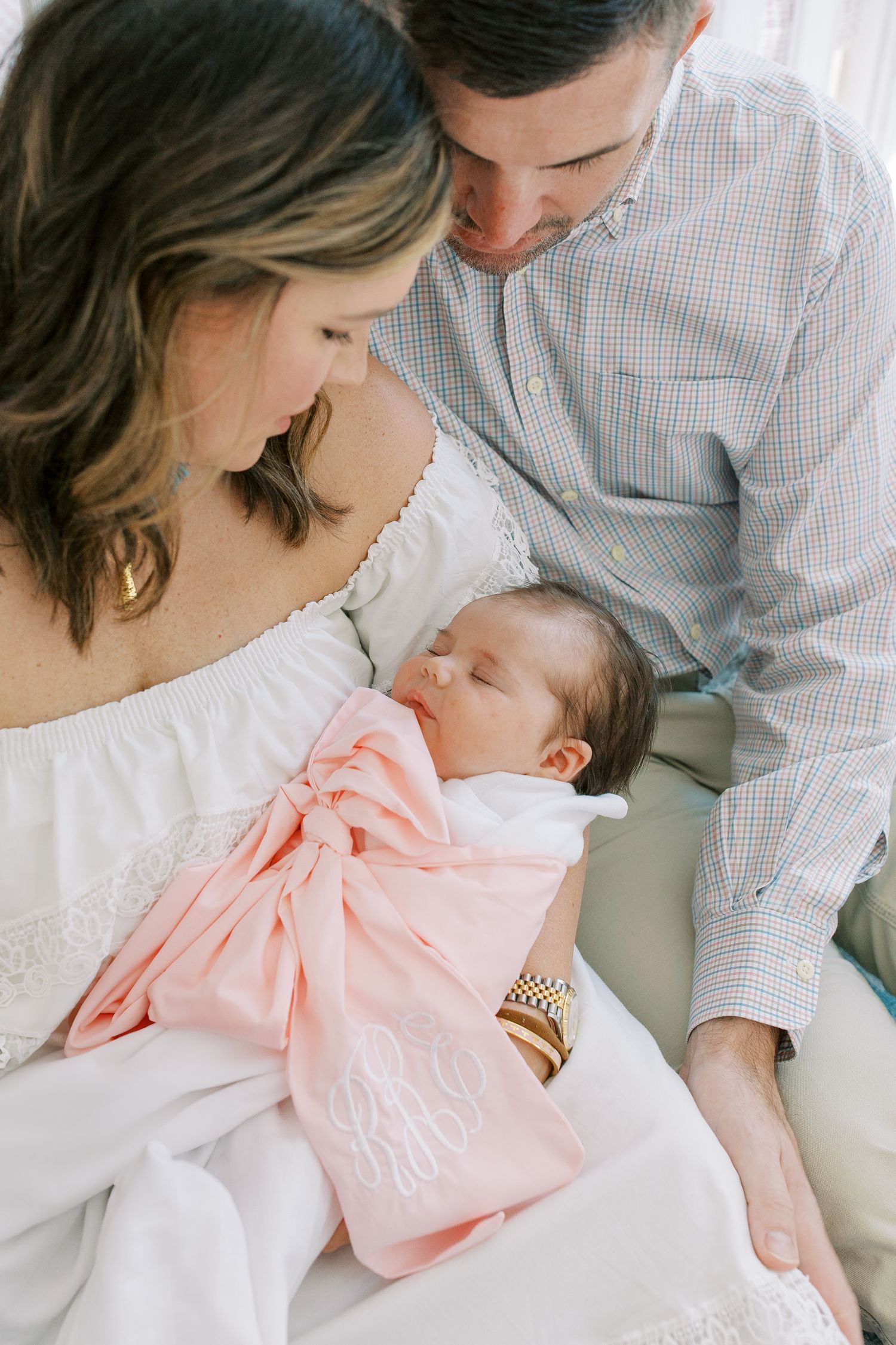 Intimate family moment captured in soft natural light with parents cradling sleeping newborn.