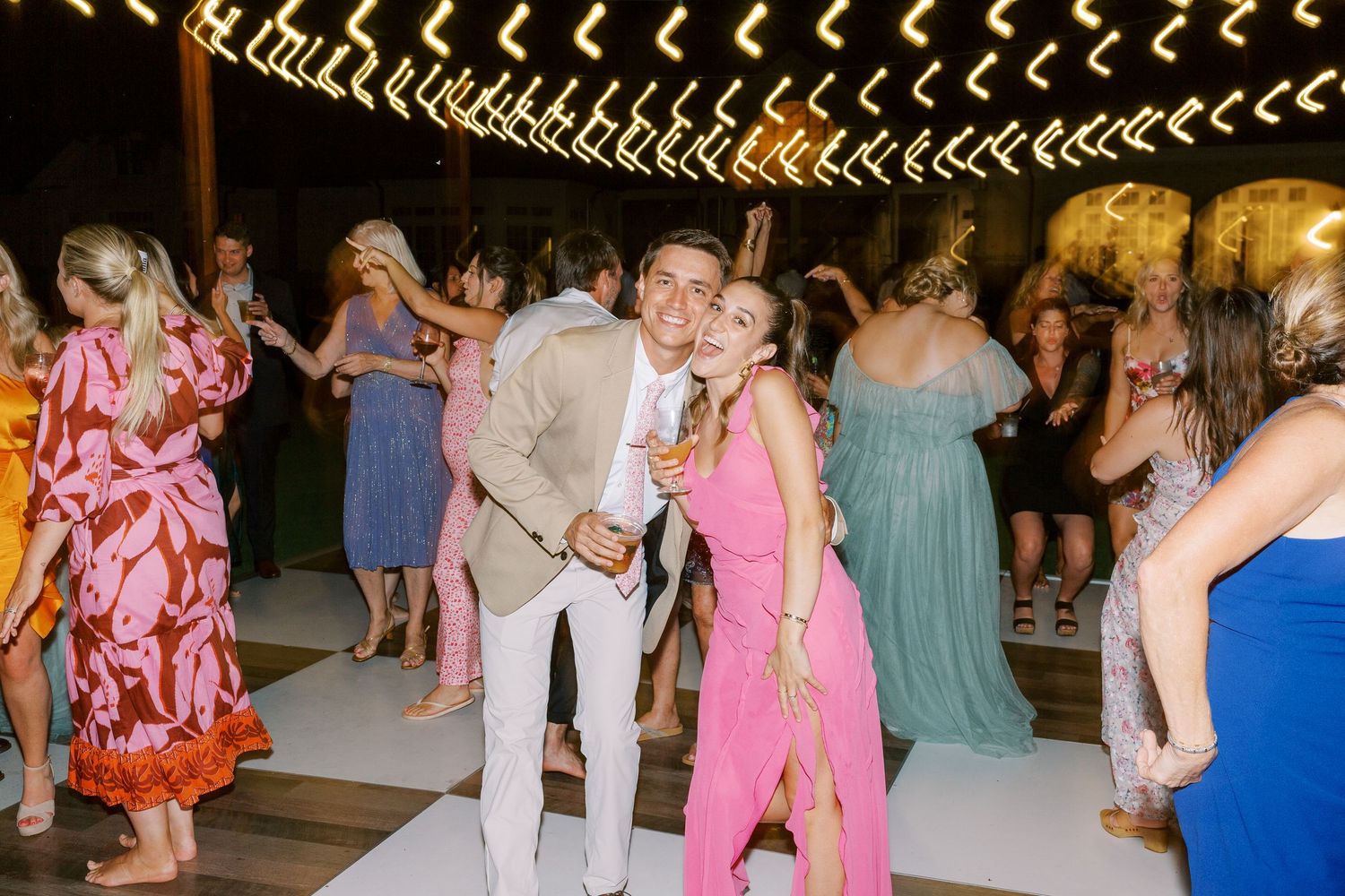 Lively wedding reception with guests dancing under decorative string lights.
