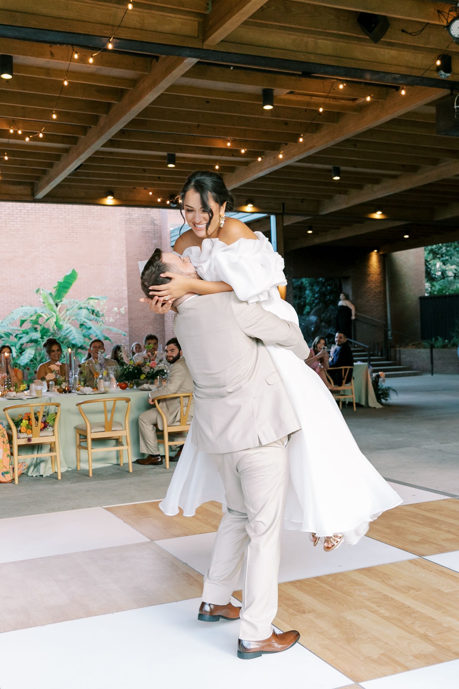 Wedding couple shares their first dance in an indoor reception venue with string lights overhead.