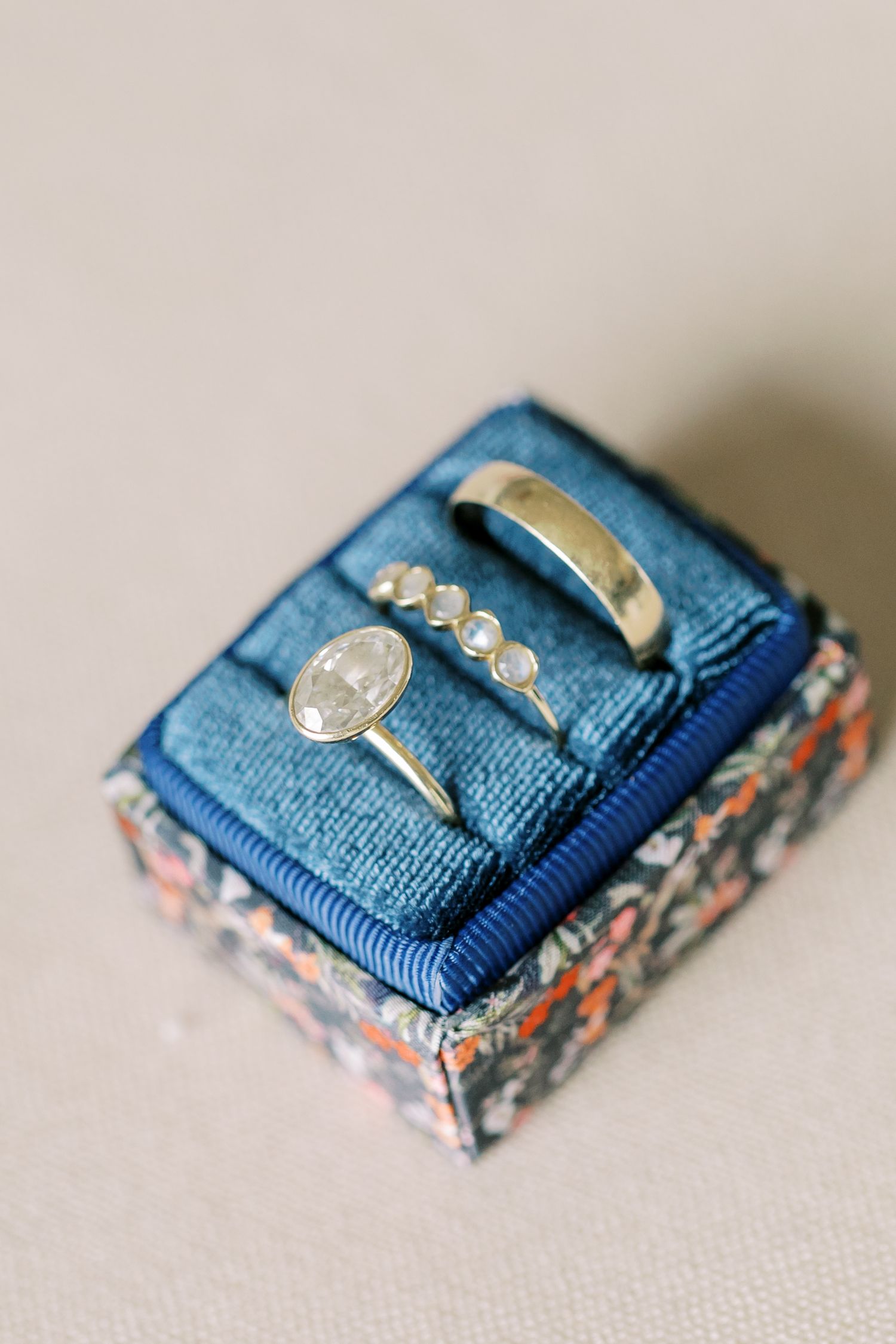 Two elegant wedding bands rest on a small blue velvet pillow with floral print detail.