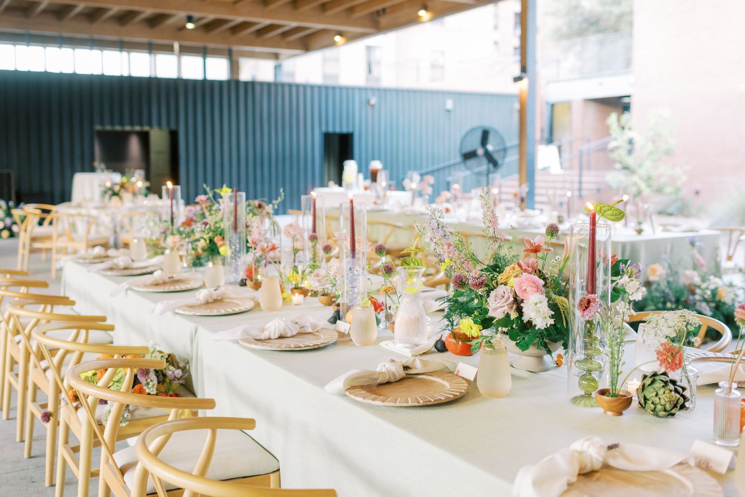 Wedding reception tables set with elegant decor and floral centerpieces in an industrial-style venue.