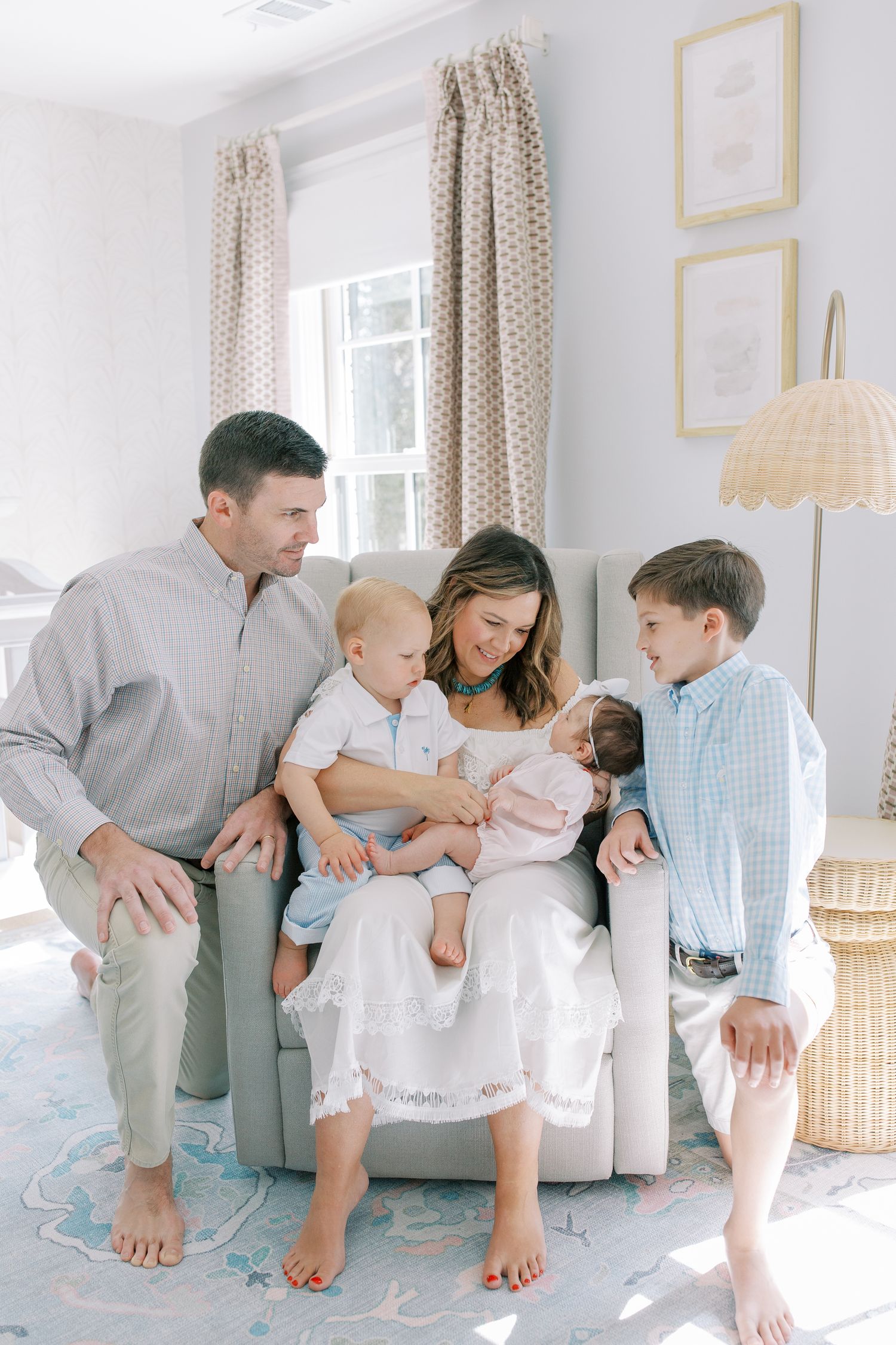 Family sitting together in a bright sunlit living room on a gray couch with polka dot curtains and framed wall art.