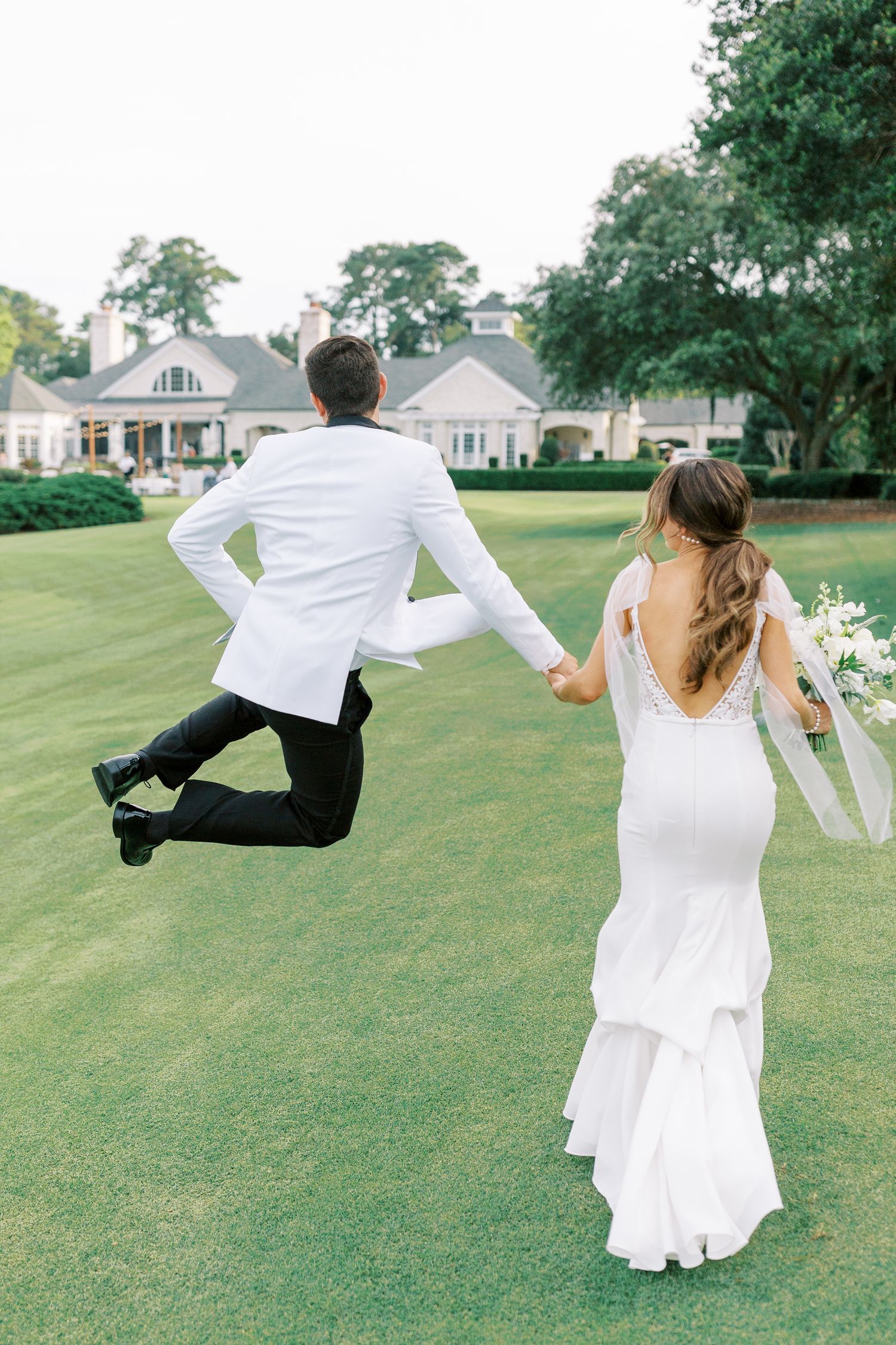Playful moment on golf course with groom leaping in white dinner jacket at Belfair Golf Course.