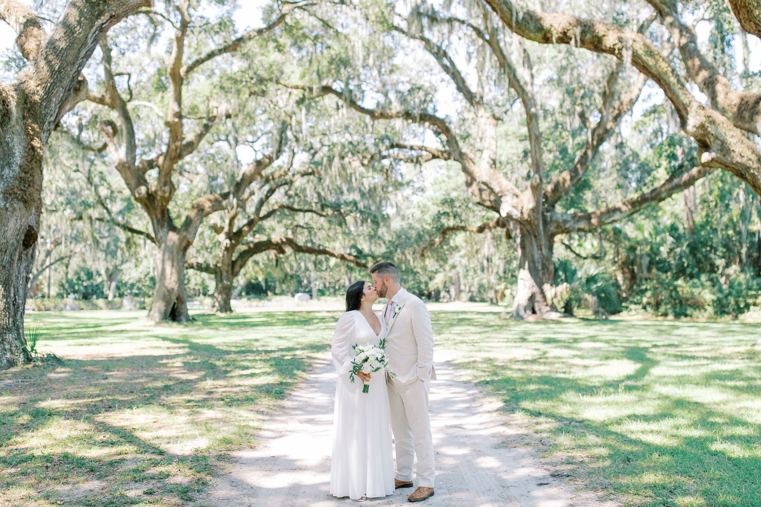 Two people in wedding attire share a moment on a pathway beneath majestic Spanish moss-draped live oak trees on Hilton Head Island, SC.