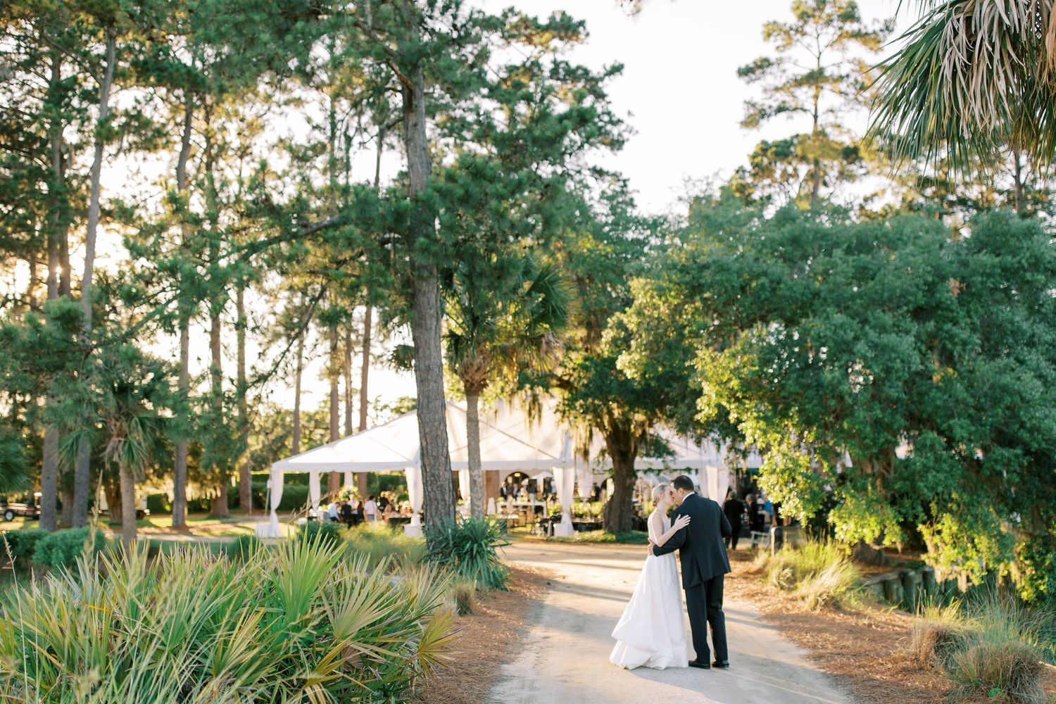 A couple walks along a scenic path under Spanish moss-draped trees at an outdoor wedding venue during golden hour at Oldfield in Okatie, SC
