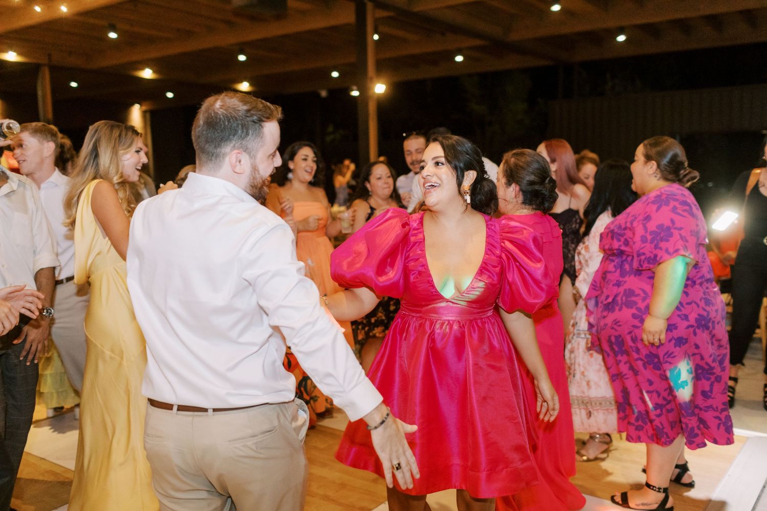A lively dance floor scene with guests in vibrant pink and colorful formal attire.