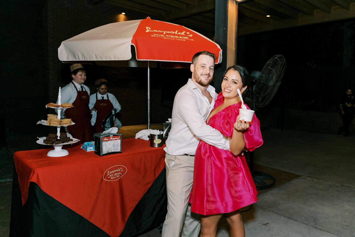 Evening wedding reception with red tablecloths and guests dancing on dance floor.