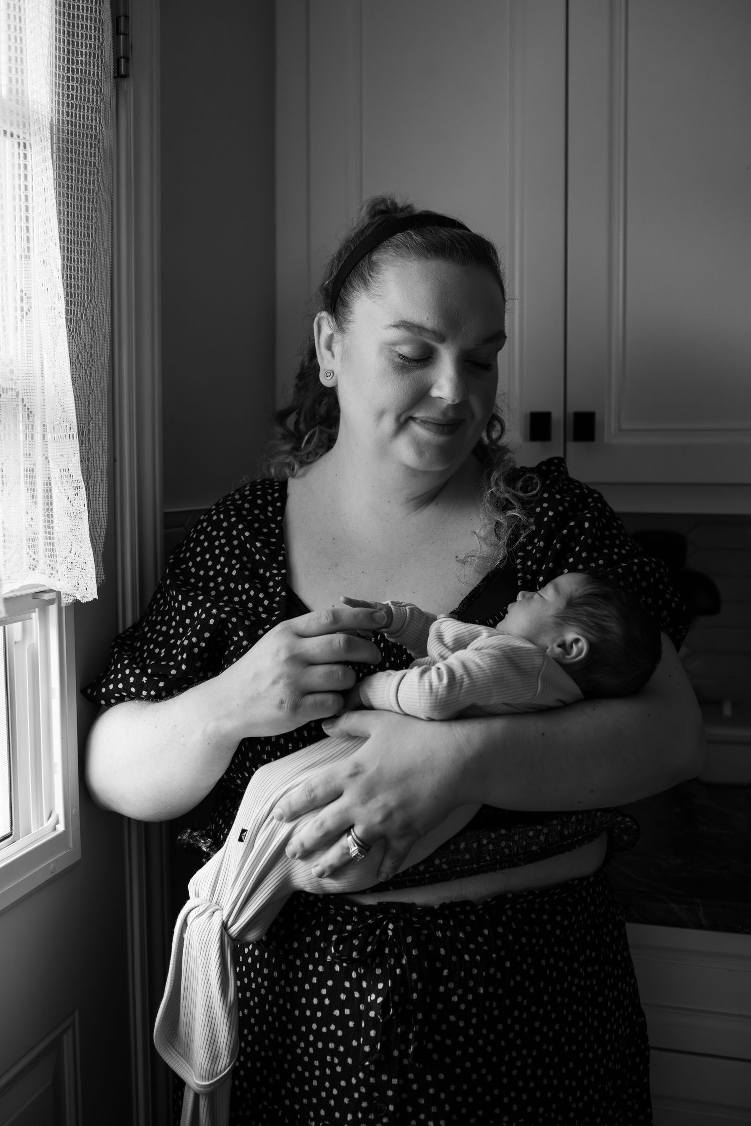 A tender black and white series of four photos showing intimate moments between parent and newborn in a kitchen setting.