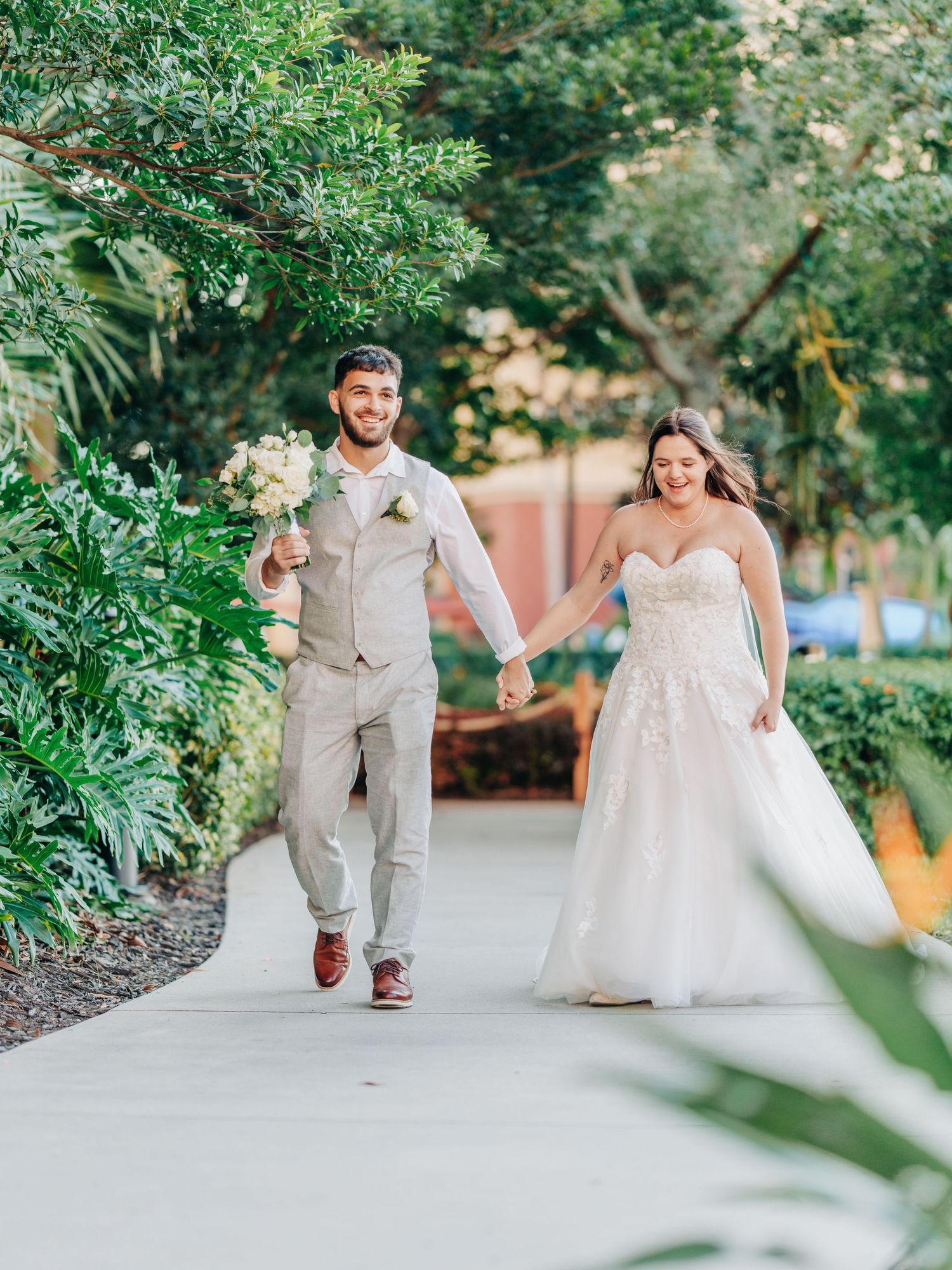 Newlyweds walking along a garden path at Wyndham Grand Orlando Resort Bonnet Creek, with lush greenery surrounding them on a sunny day.