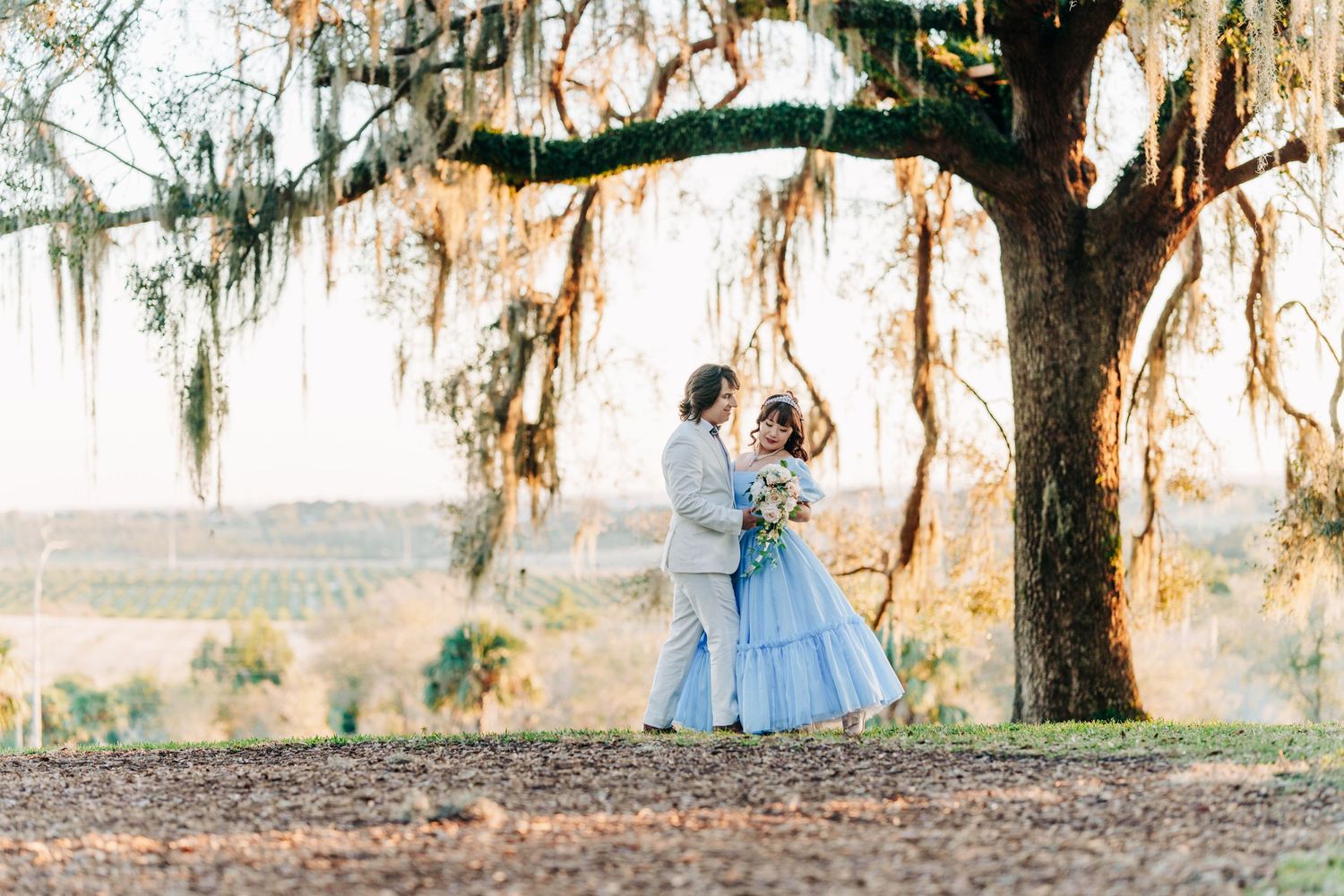A romantic couple in vintage attire dance beneath a majestic Spanish moss-draped oak tree at golden hour.