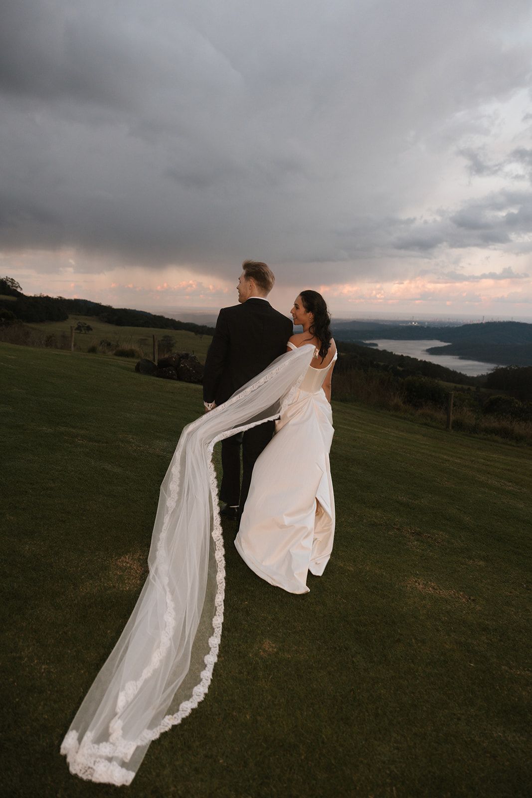 A figure in a white dress and flowing veil stands dramatically against a moody mountain landscape at sunset.