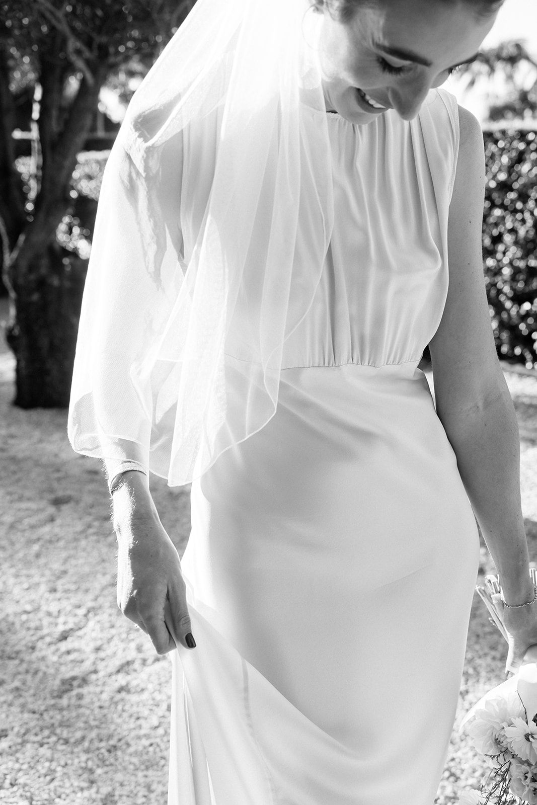 Black and white detail shot of an elegant wedding dress with a flowing veil and fitted waistline.