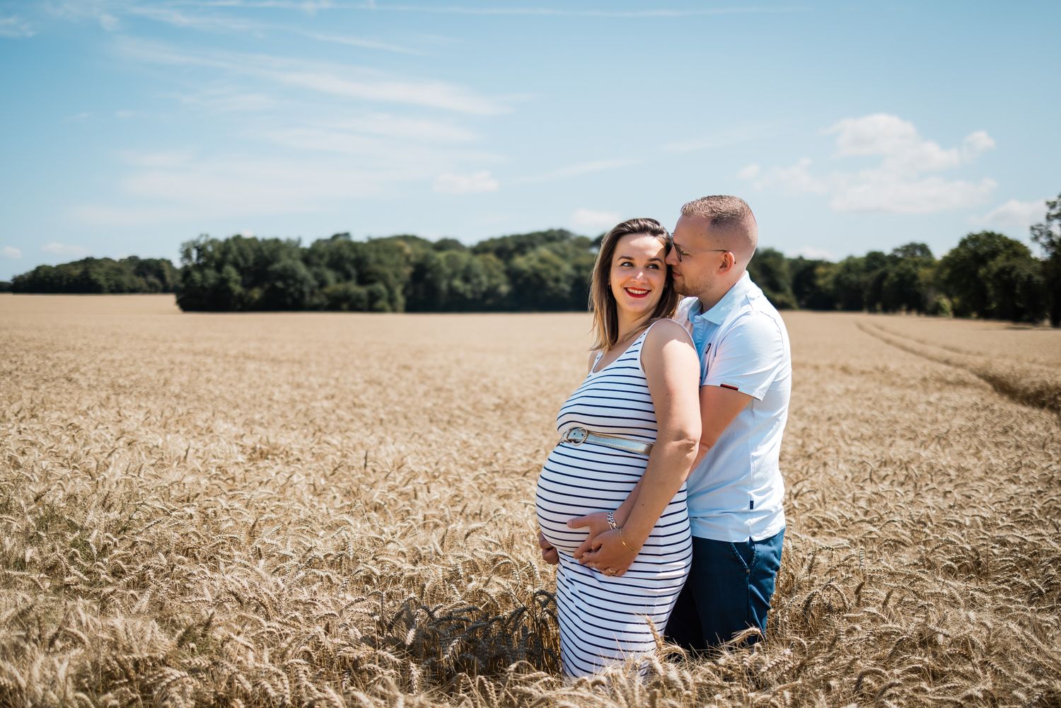 Un couple en tenues rayées assorties se tient ensemble dans un champ de blé doré par une journée d'été ensoleillée.