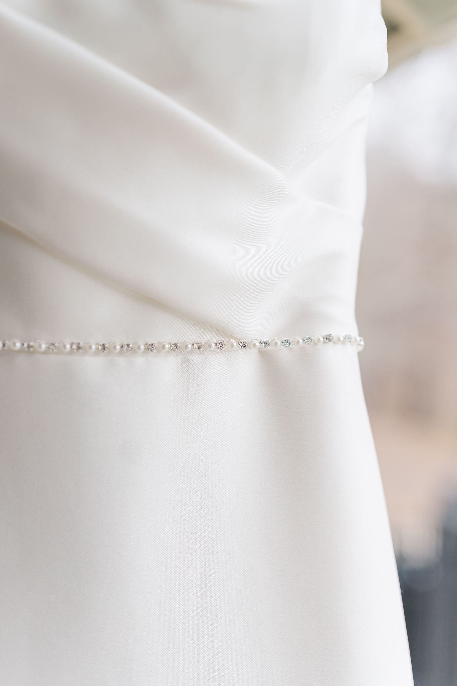 A close-up of a white wedding dress with delicate pearl beading detail along the waistline.