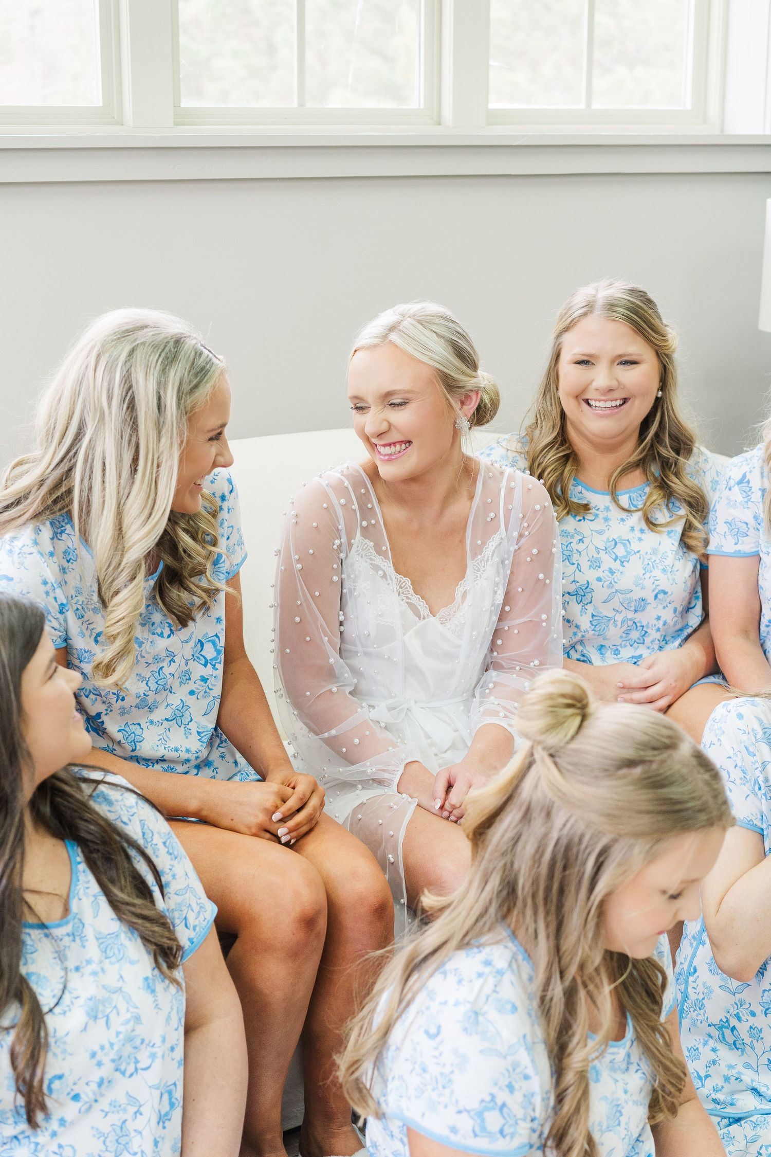 A group in matching blue floral dresses sits together and shares a joyful moment with someone wearing white lace.
