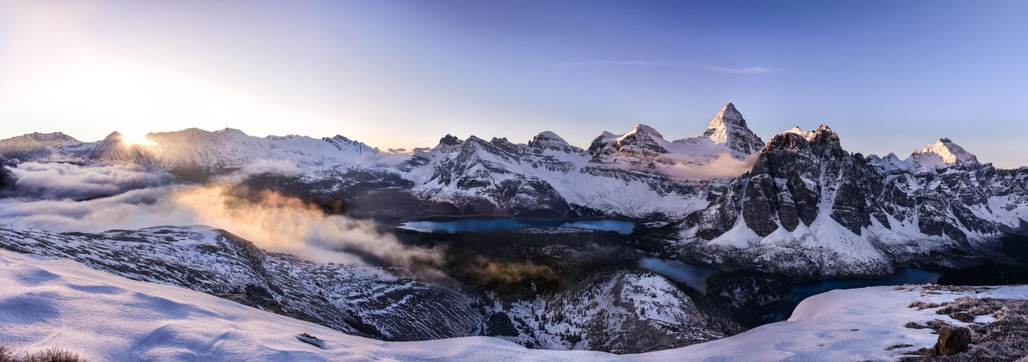 Panoramic winter mountain landscape with dramatic peaks and misty valleys at dawn.