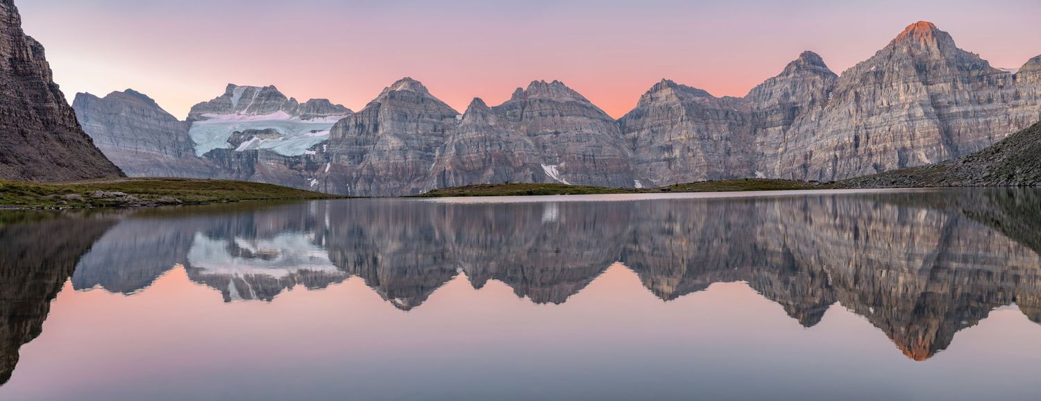 Mountain range perfectly reflected in calm lake waters during pink sunset.
