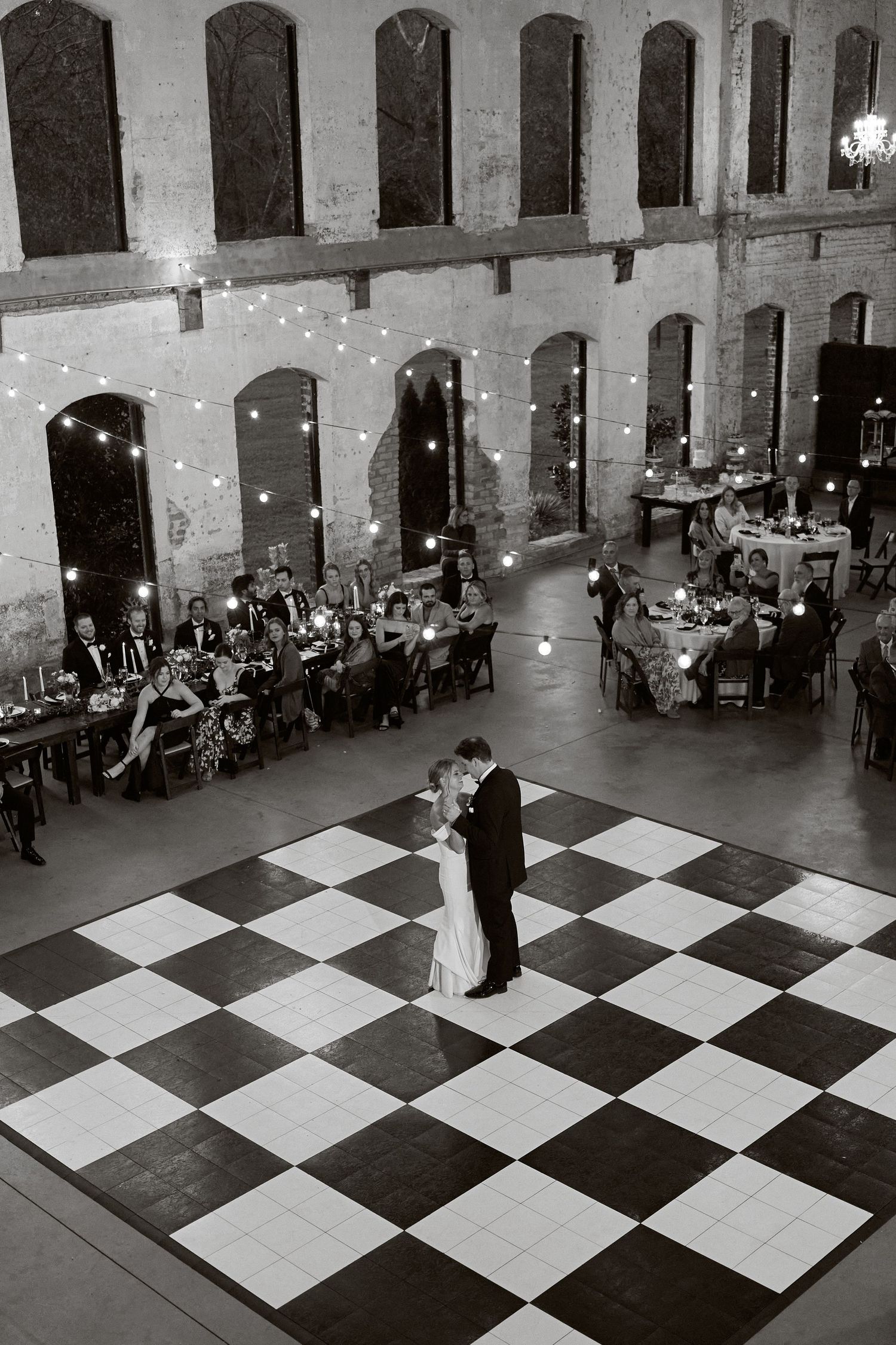 Overhead view of first dance on checkered ballroom floor with guests dining at historic venue.