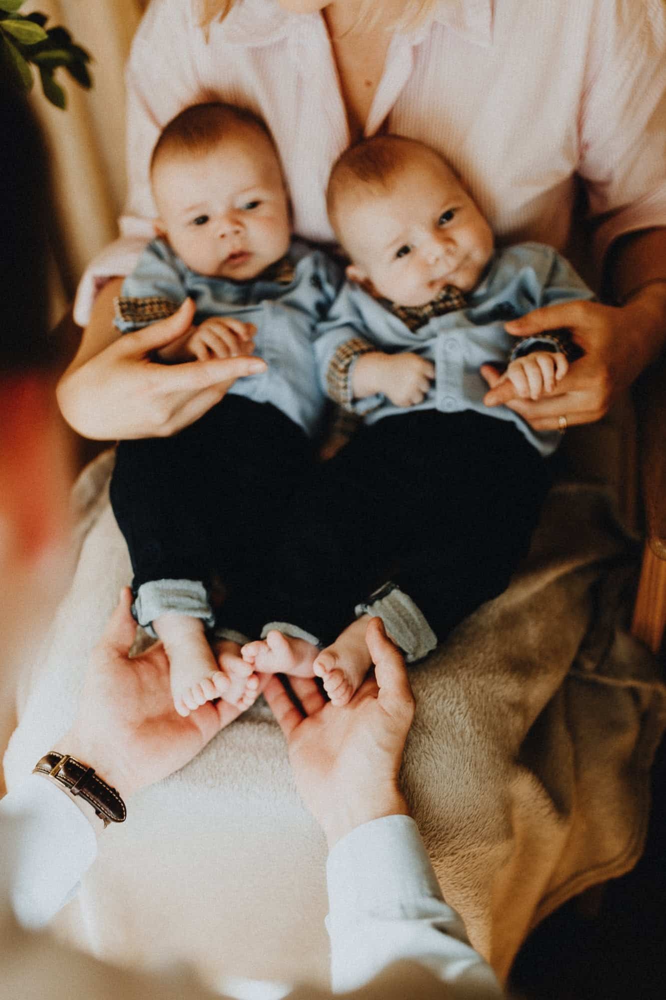 Twee baby’s in blauwe outfitjes op schoot tijdens een lifestyle shoot in West-Vlaanderen. Hun voetjes worden liefdevol vastgehouden.