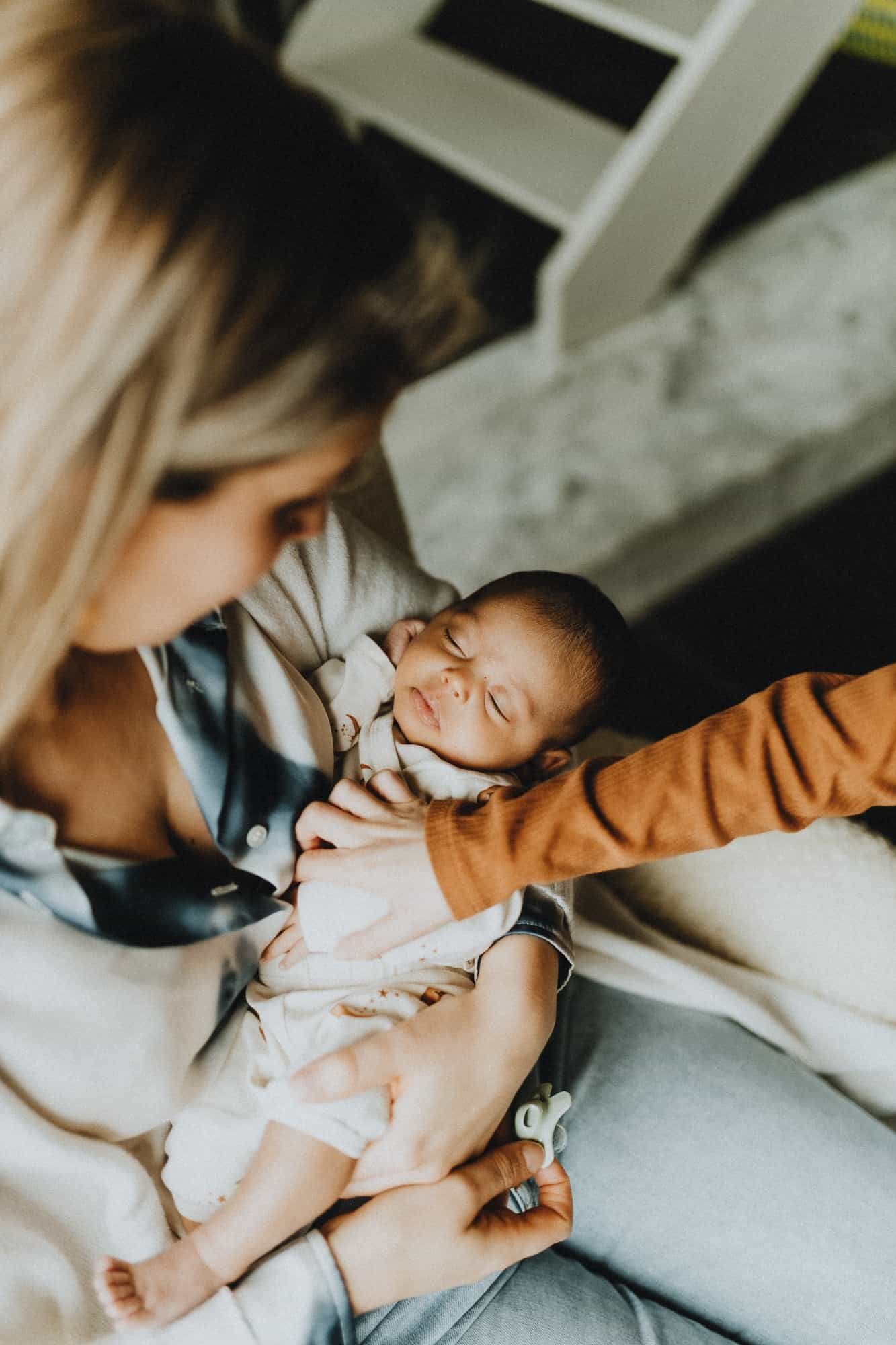 Een vrouw wiegt haar slapende baby in haar armen tijdens een lifestyle newborn shoot in Kortrijk. Intiem en teder moment.