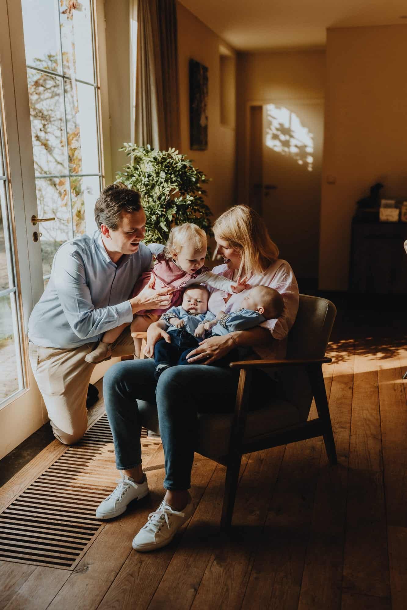 Lifestyle gezinsmoment in Brugge: ouders spelen liefdevol met een peuter en twee baby’s bij het raam. Warme sfeer en daglicht.