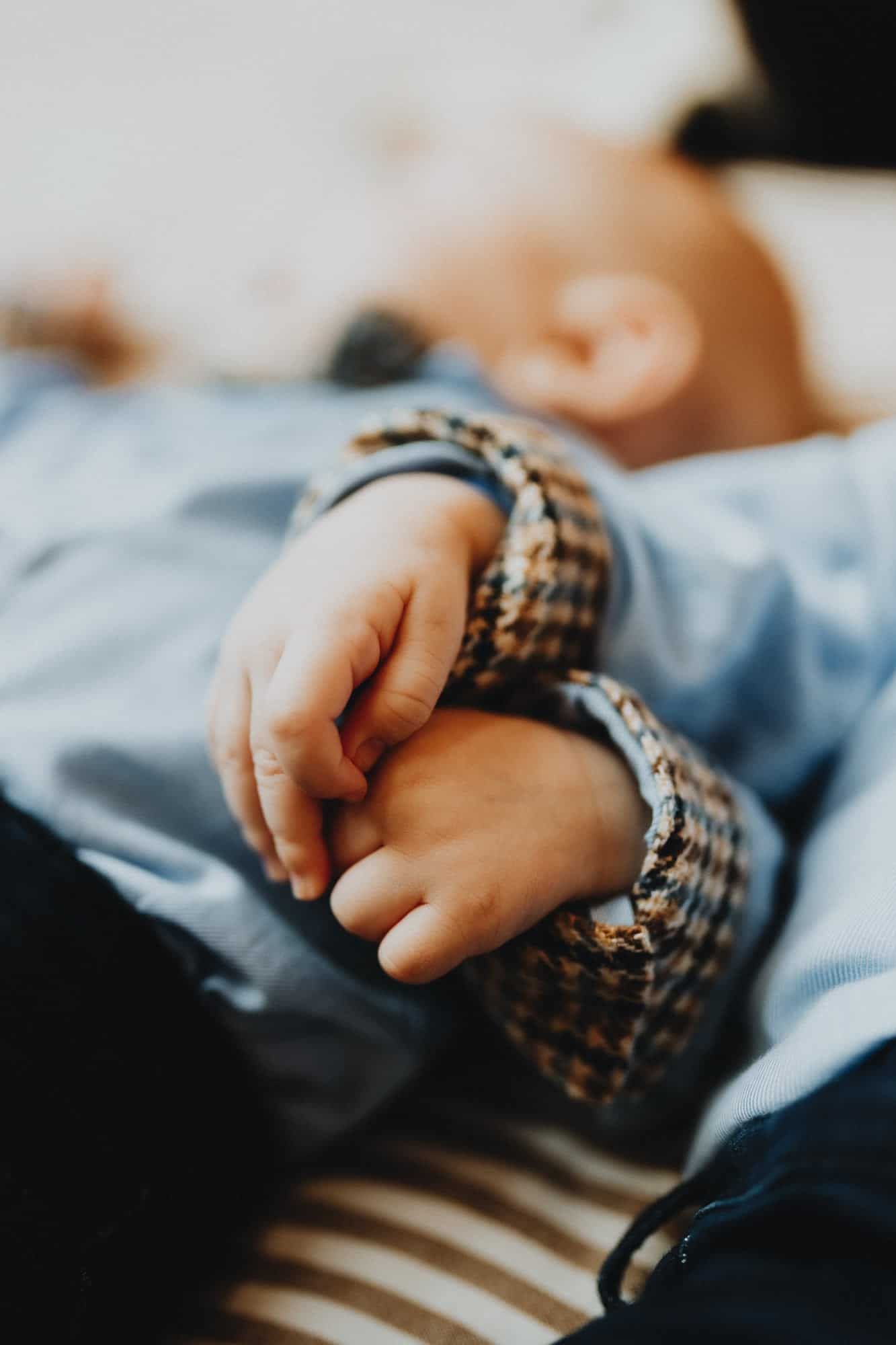 Detailopname tijdens newbornshoot in Brugge: babyhandje houdt een volwassen vinger vast. Het kindje draagt een blauw hemdje.