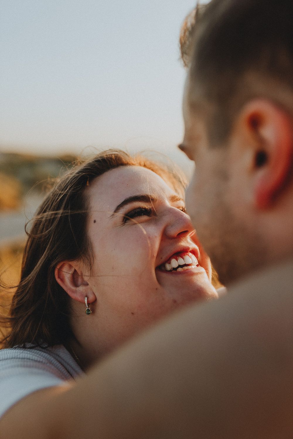 Vrouw kijkt stralend naar haar partner in een intiem moment, met zonlicht dat haar gezicht warm verlicht.