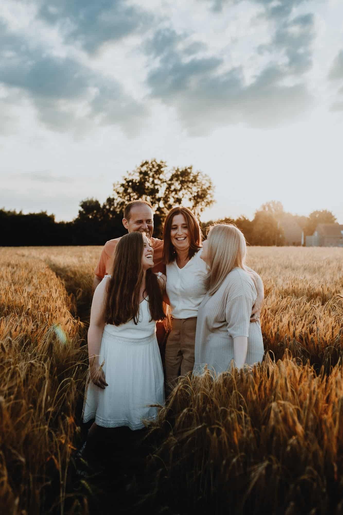 Een gezin van vier staat samen in een gouden tarweveld bij zonsondergang. Ze lachen en omhelzen elkaar in een warme, dromerige sfeer.