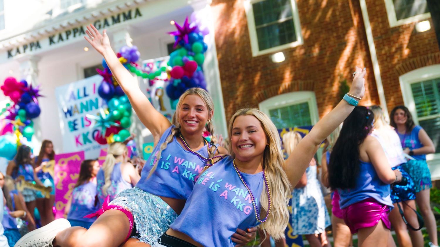 Colorful crowd celebrates with confetti and balloons at outdoor festival in daylight with joyful expressions.