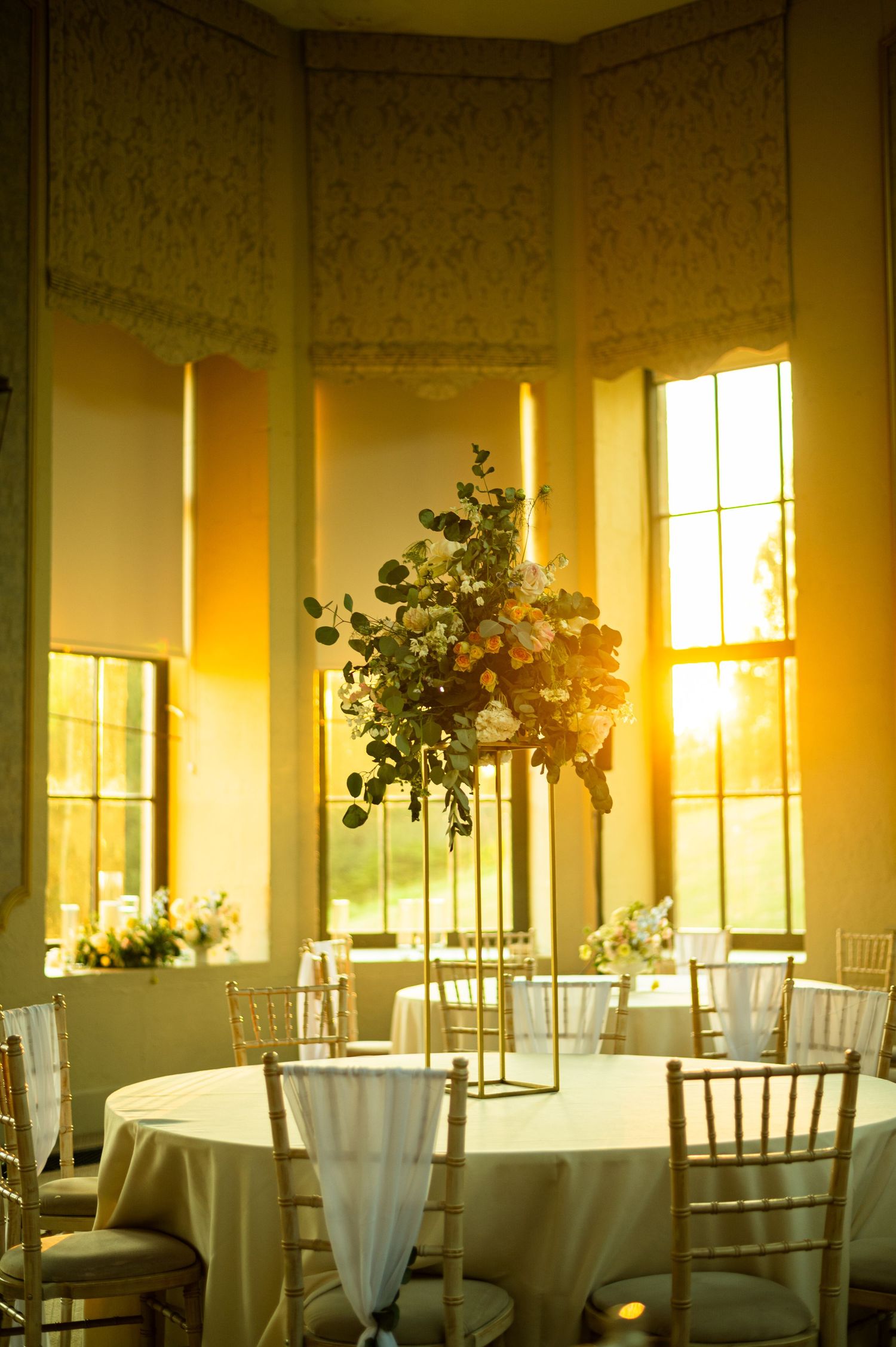 Elegant wedding reception venue with sunlit windows and white table settings.