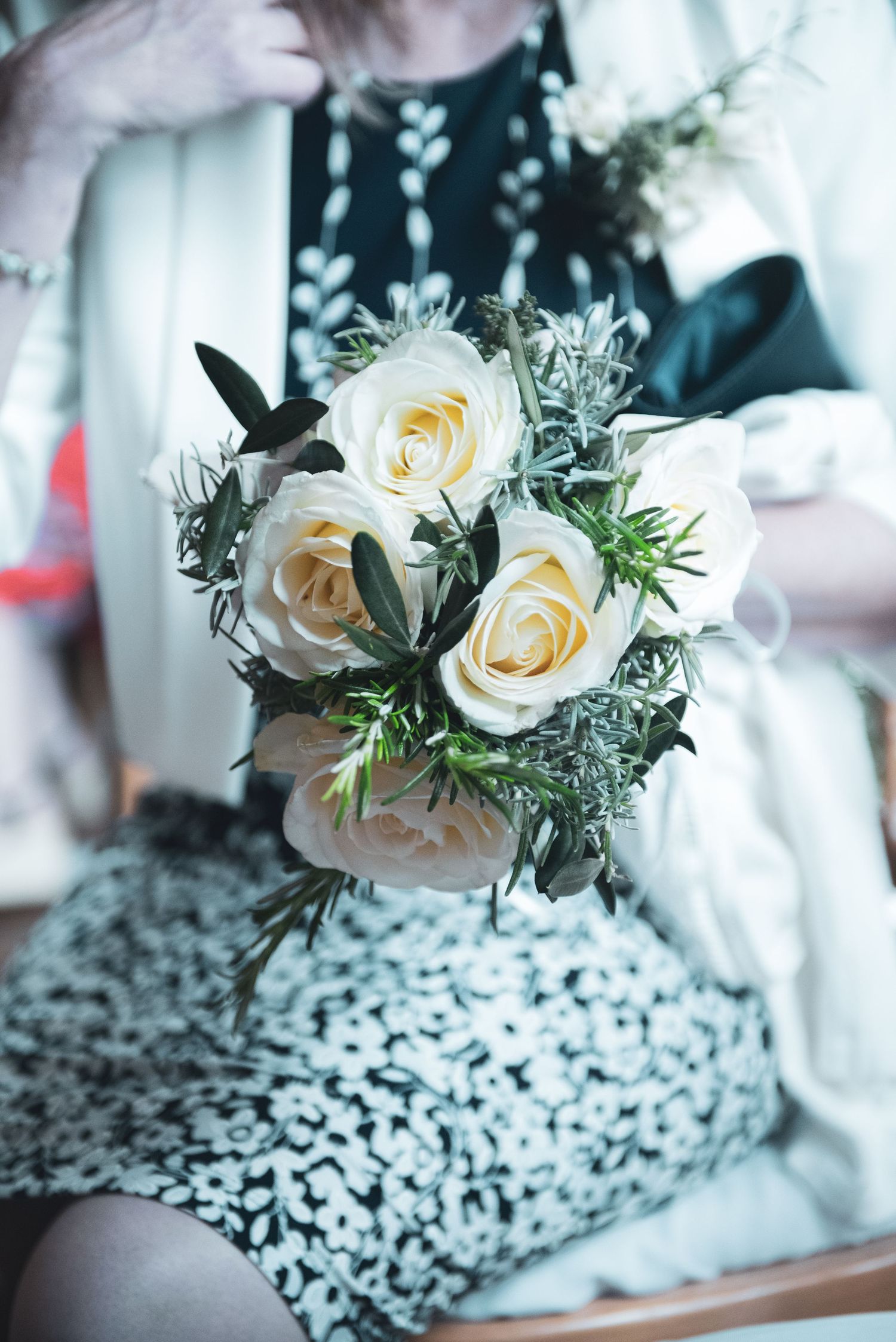 Delicate white rose wedding bouquet with greenery accents on patterned fabric.