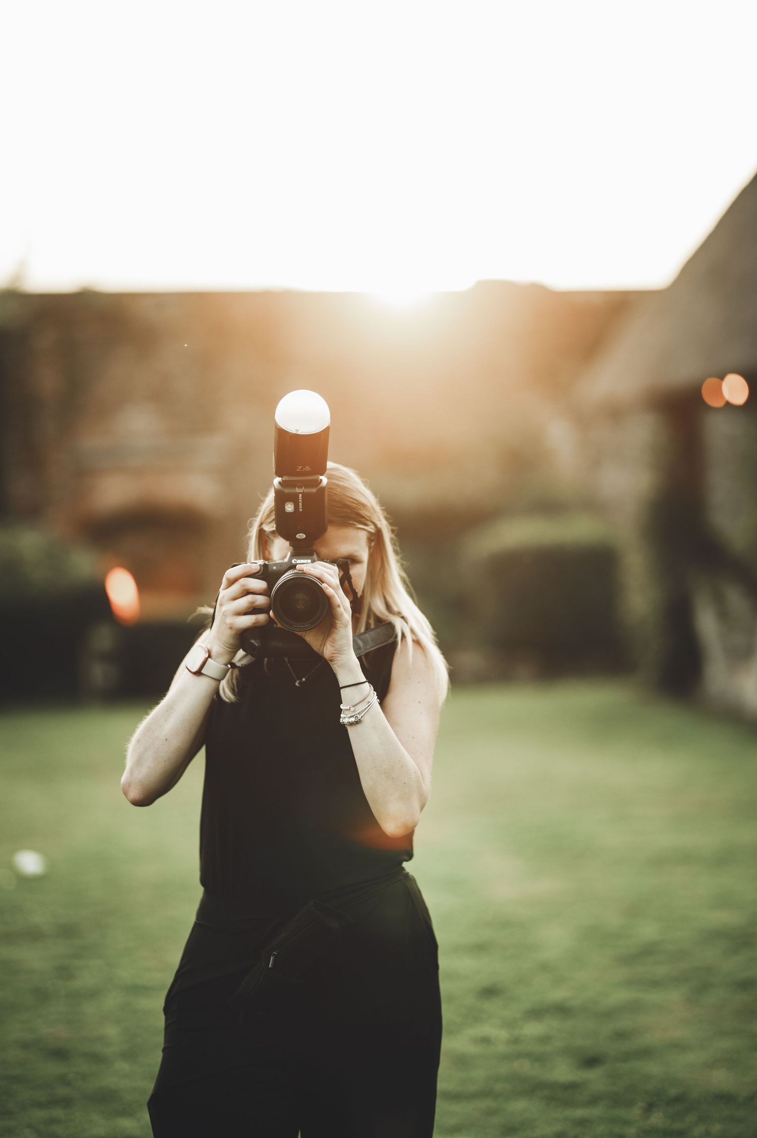 Photographer holding camera in outdoor golden sunlight with bokeh effect and green lawn in background.