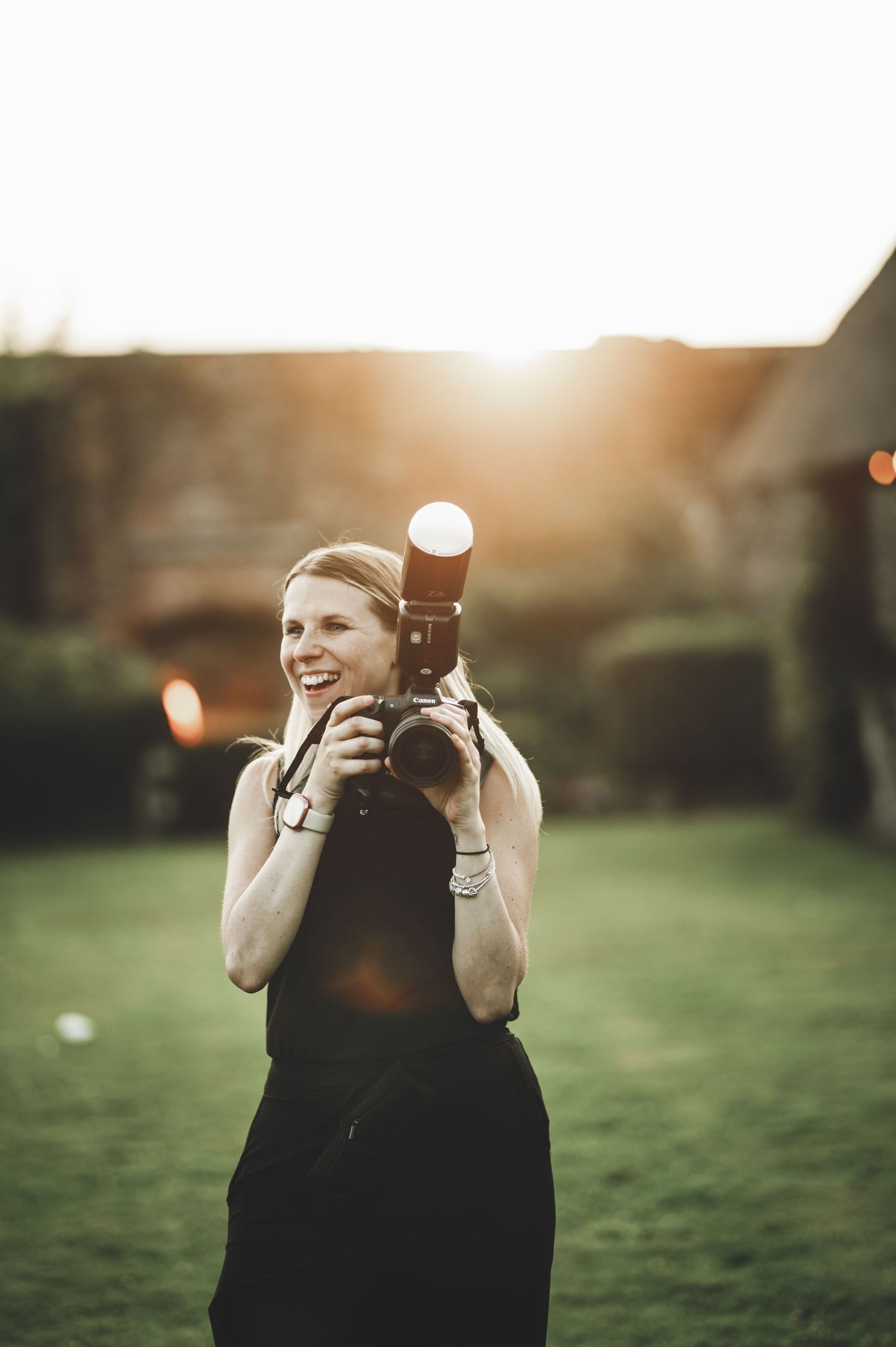 Photographer holding a professional DSLR camera while standing in a grassy field during golden hour sunset.