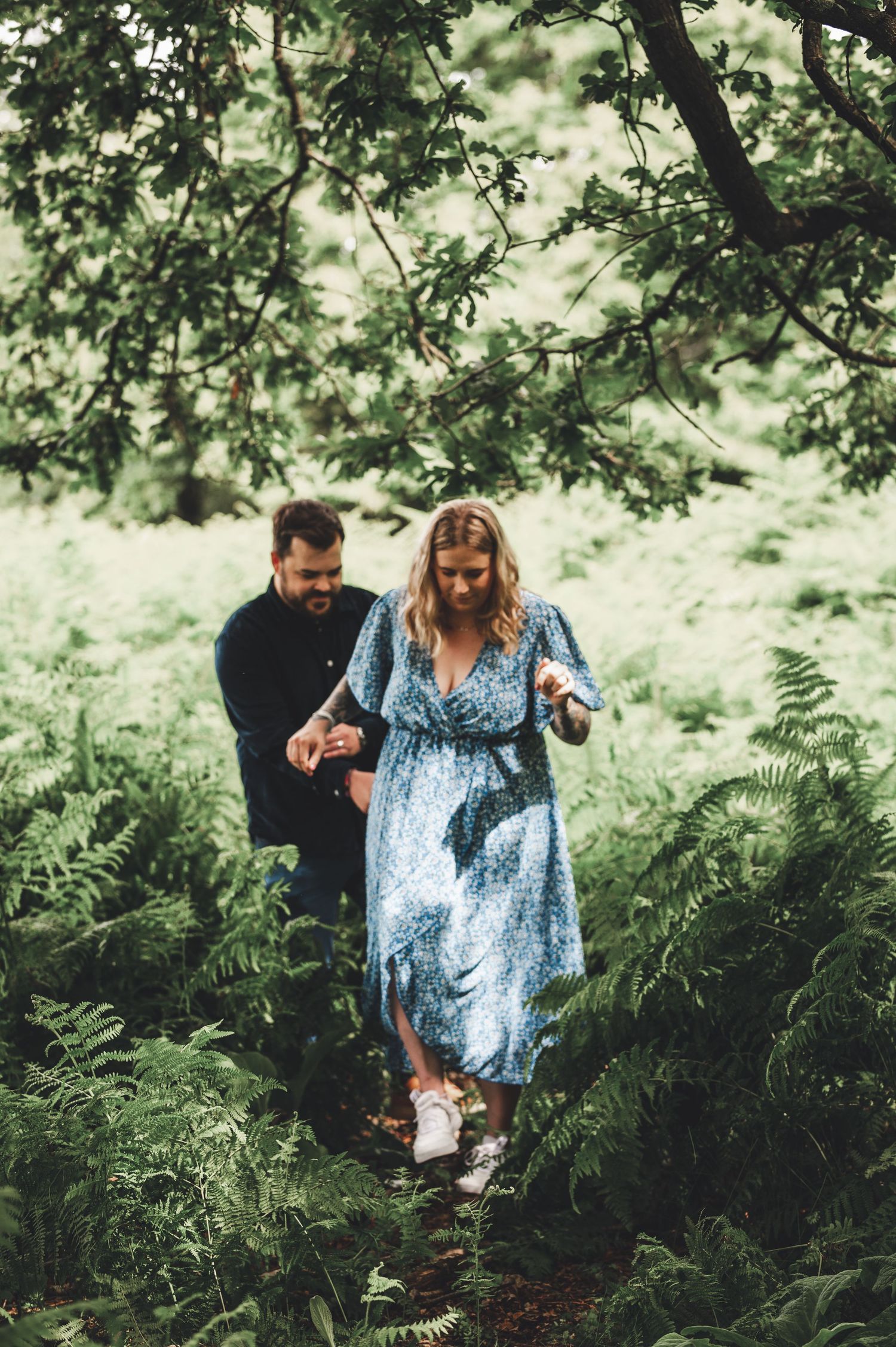 Couple walking through lush ferns and trees during outdoor photo session.