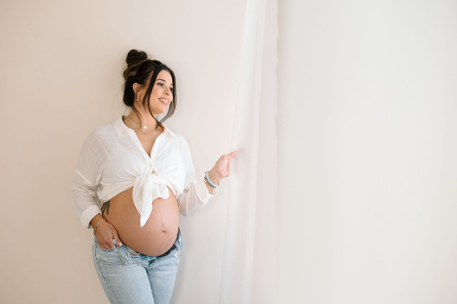 Maternity photo featuring white knotted top and casual denim against light backdrop.