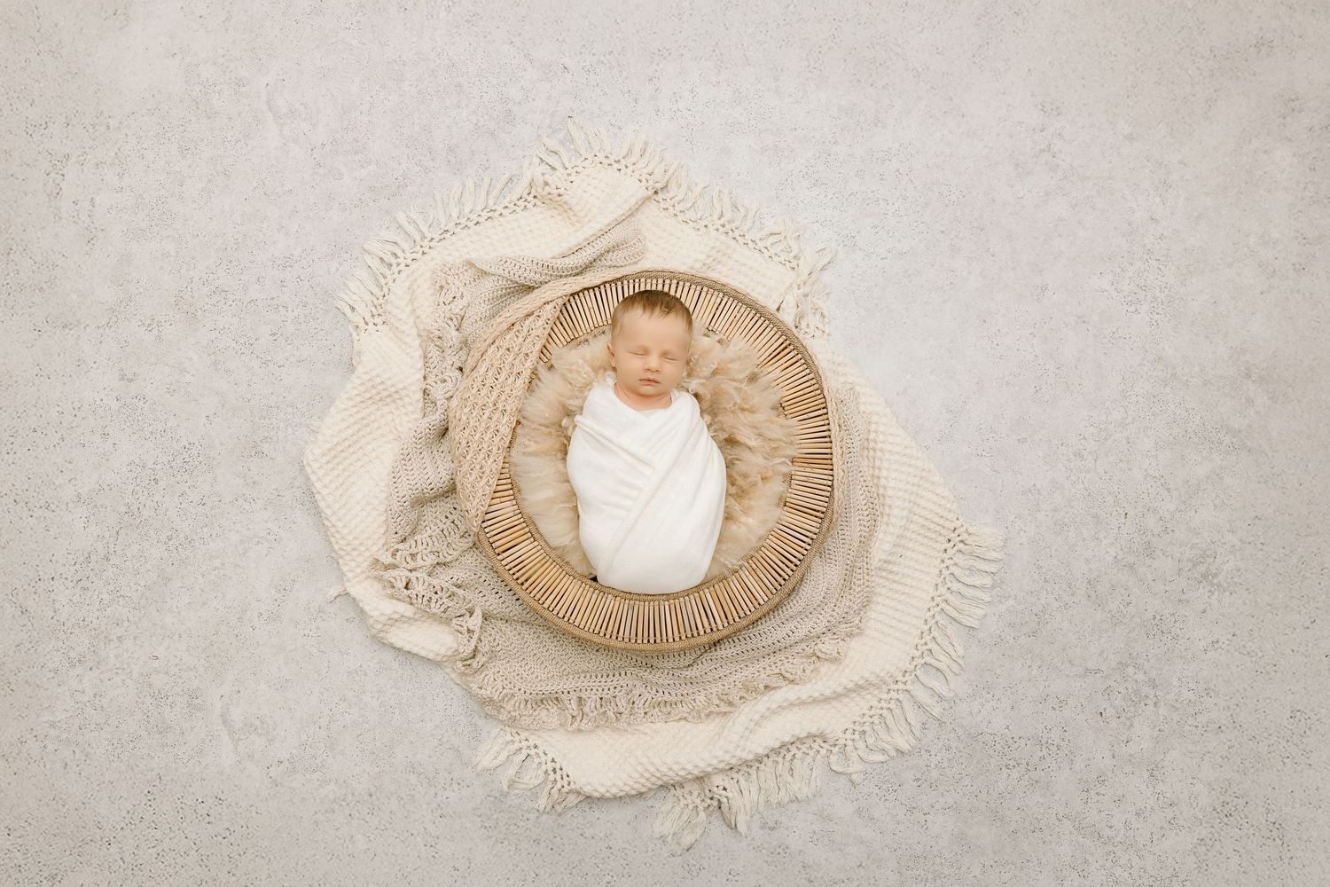 Newborn baby sleeps in round basket with textured cream fabrics.