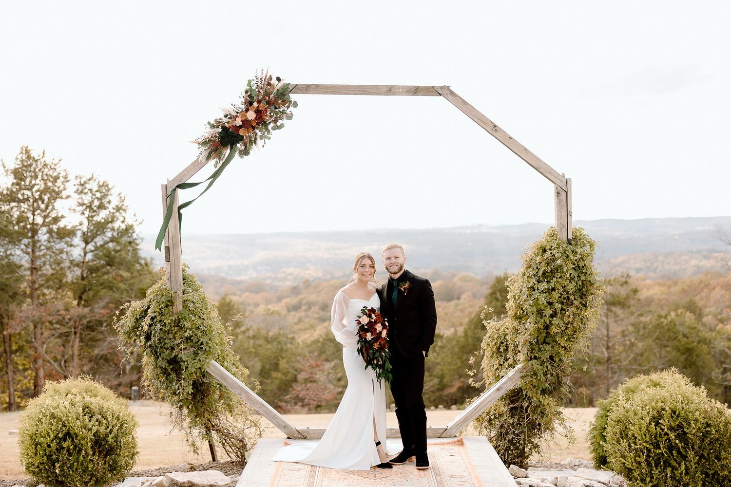 Couple stands under hexagonal wedding arch with mountain views and floral arrangements.