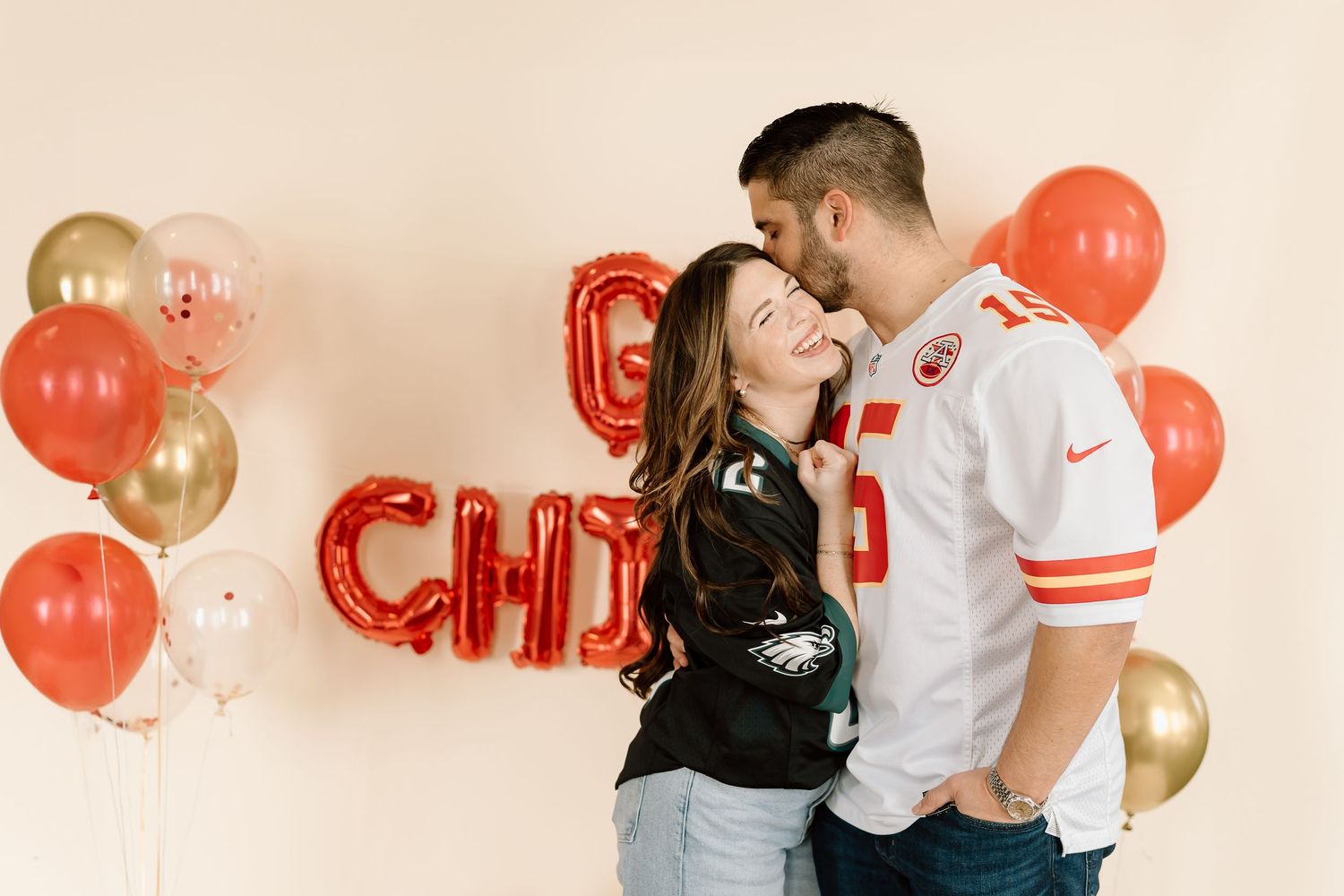 Couple posing with red and gold balloons and letter decorations at celebration.