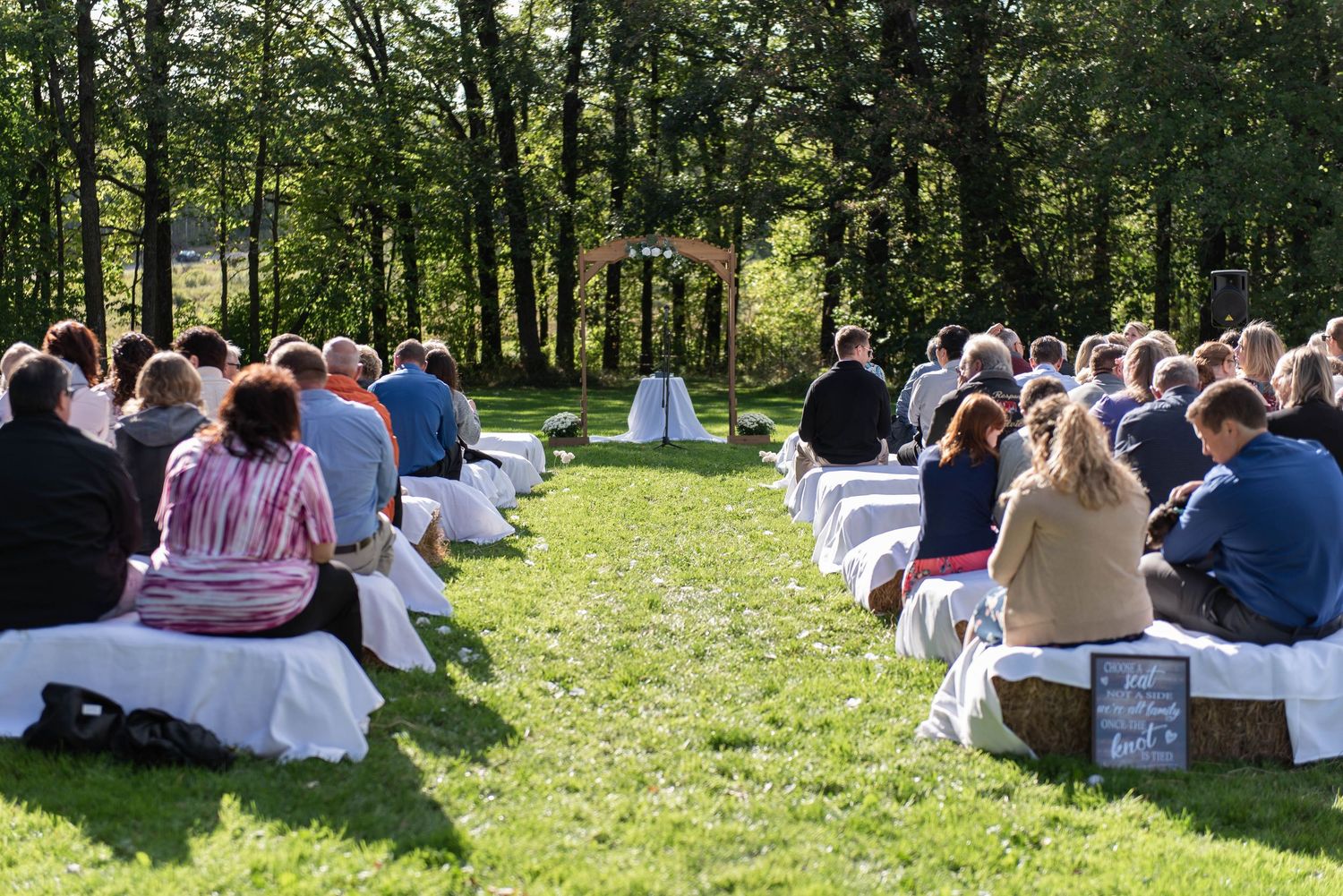 Wedding guests seated on the grass for an outdoor ceremony in a wooded area. Rum River Barn Milaca Minnesota Weddings
