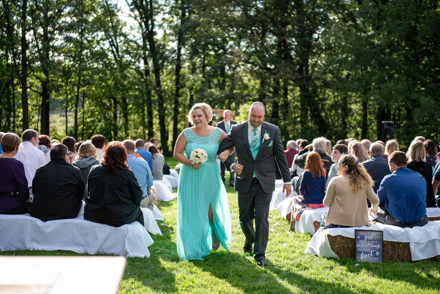 Wedding ceremony guests seated on white chairs in sunny outdoor garden setting. Rum River Barn Milaca Minnesota Weddings