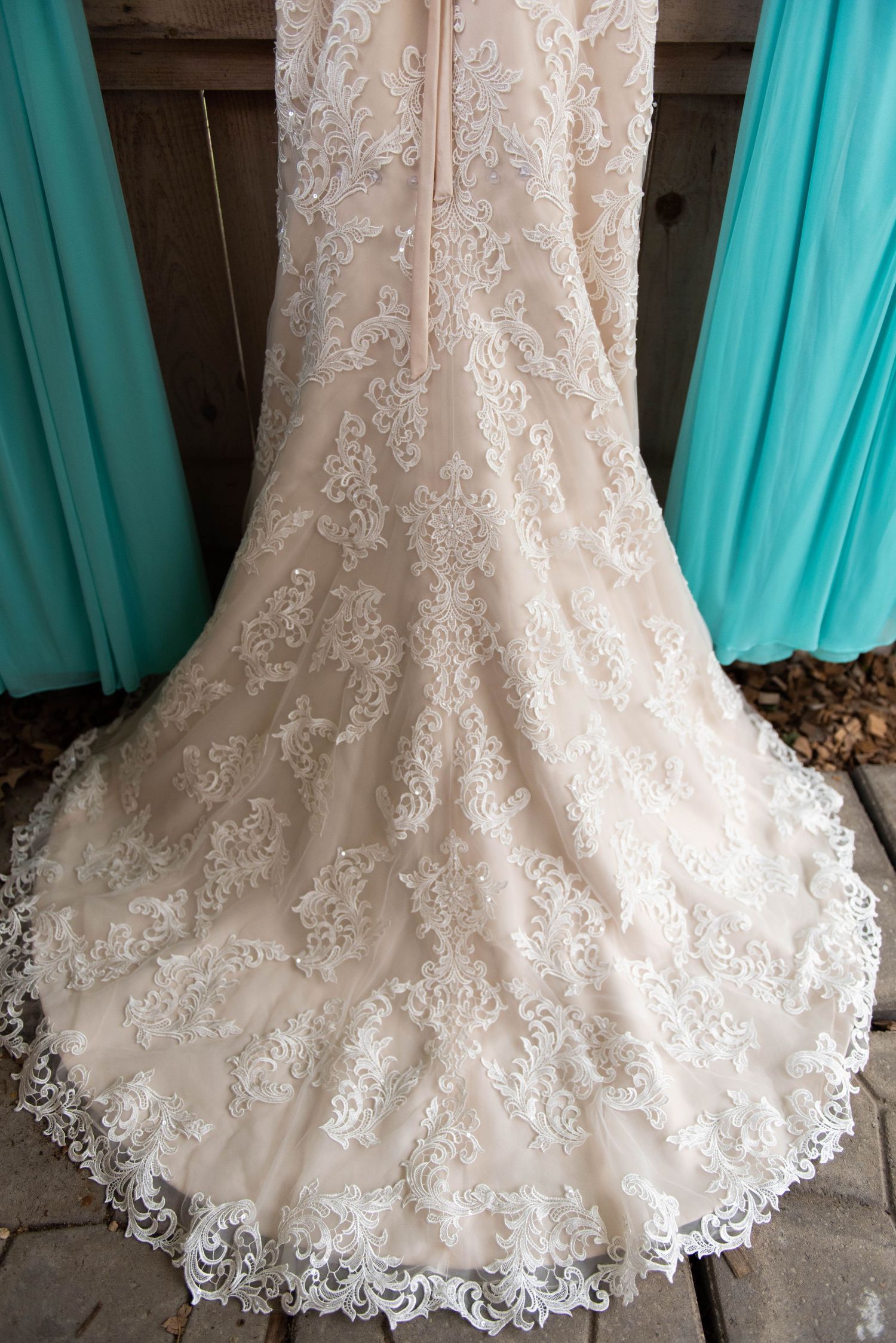 Close-up detail of a white lace wedding dress hem with intricate embroidery against turquoise backdrop.