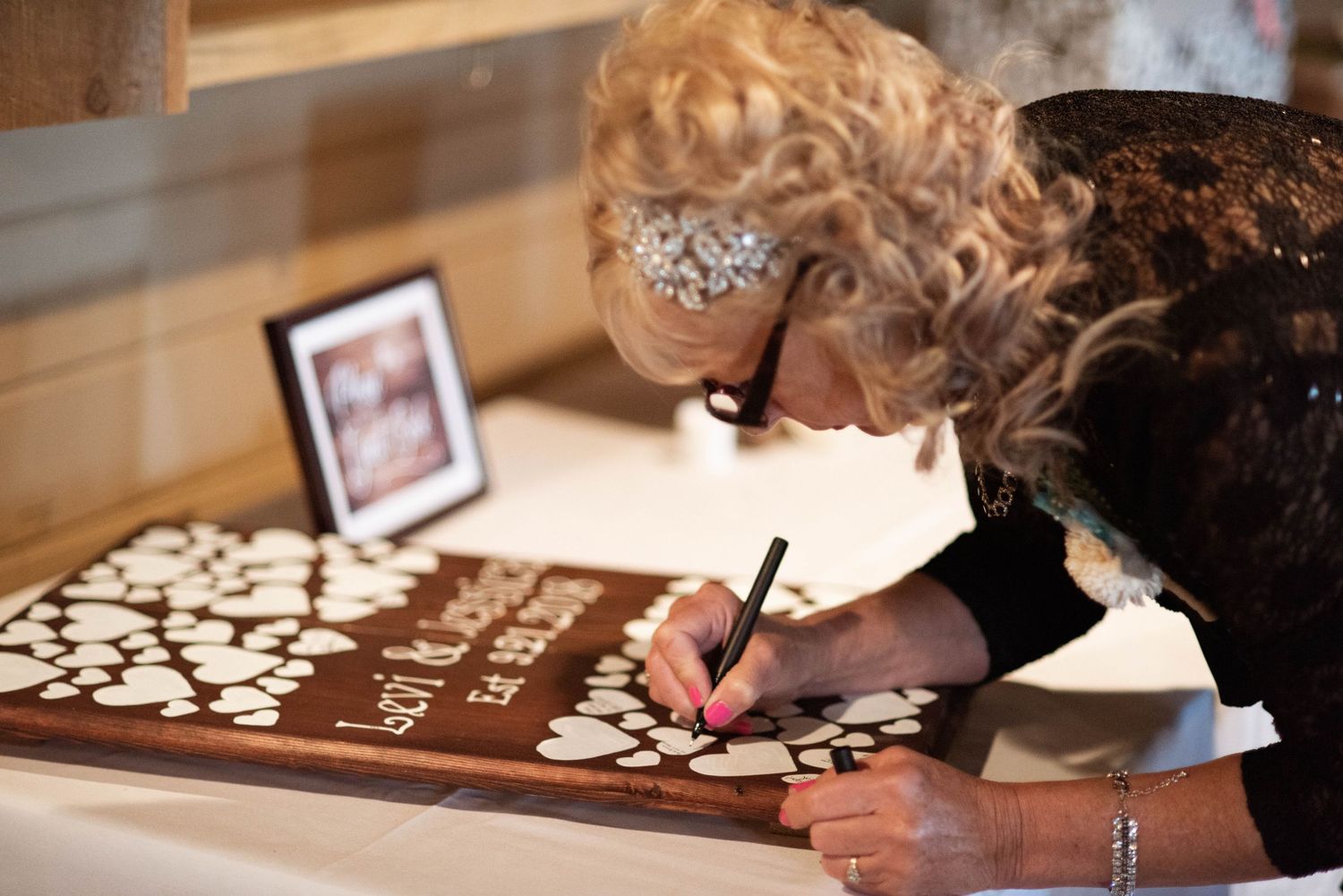A person signs a wedding guest book with wooden hearts while wearing formal attire at an elegantly decorated table.