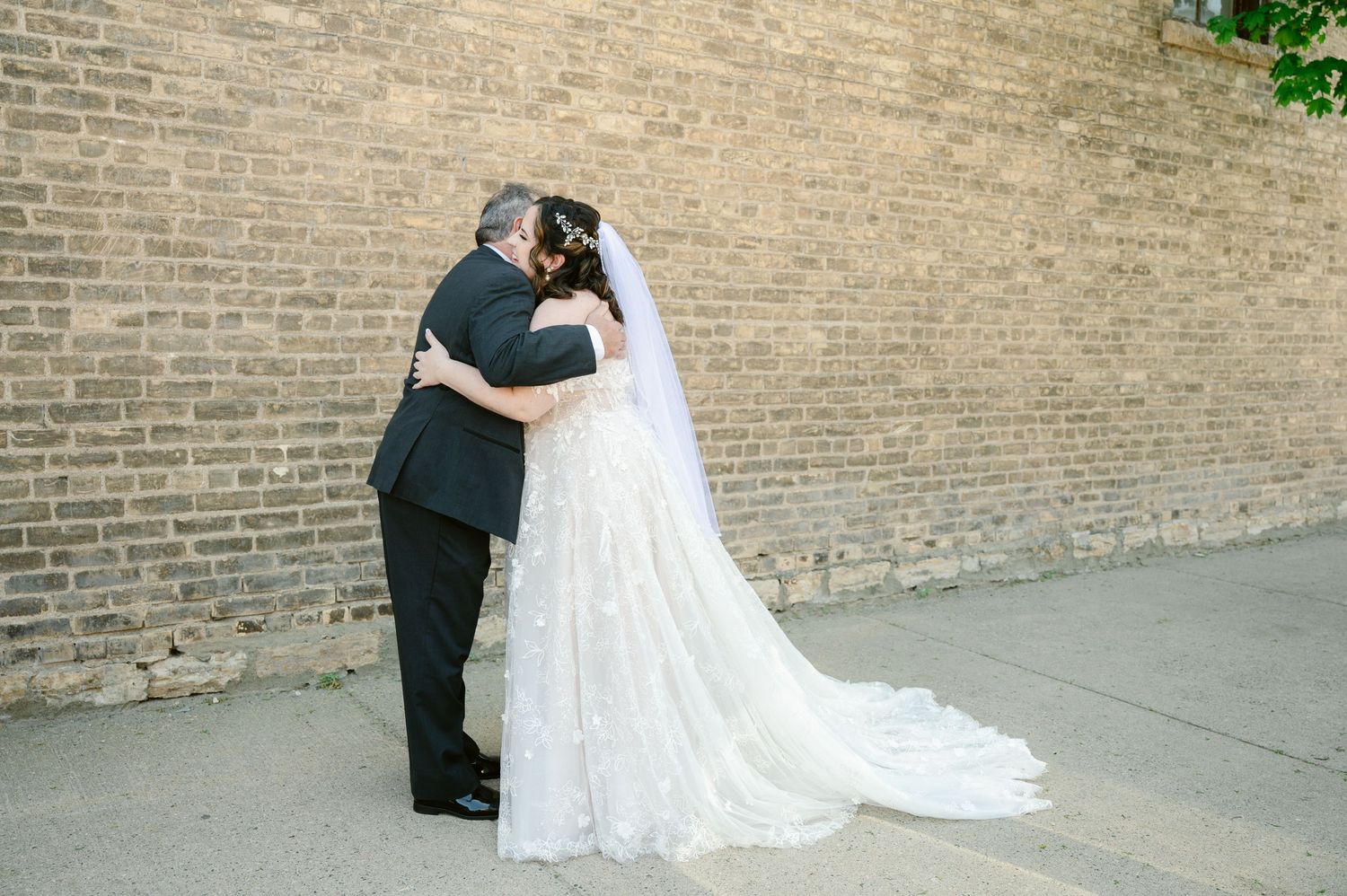 Couple embraces against a brick wall for romantic wedding portraits.