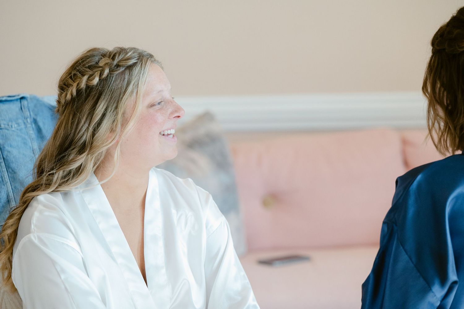A person with braided hair in a white robe smiles joyfully while getting ready.