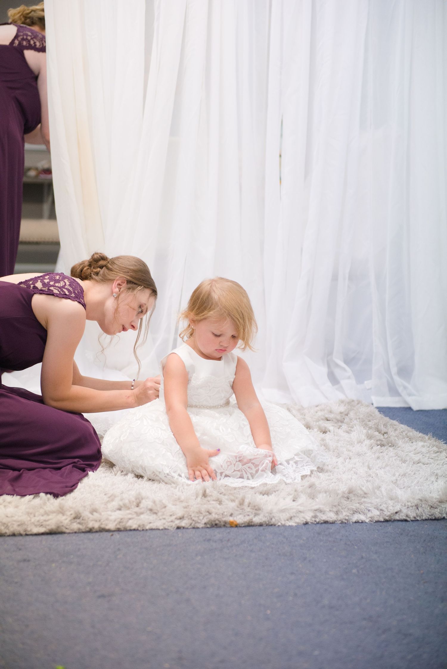 A bride in a lace wedding dress and veil adjusts her dress while getting ready on a carpeted floor. Andover wedding at Magestic Oaks Golf Cl