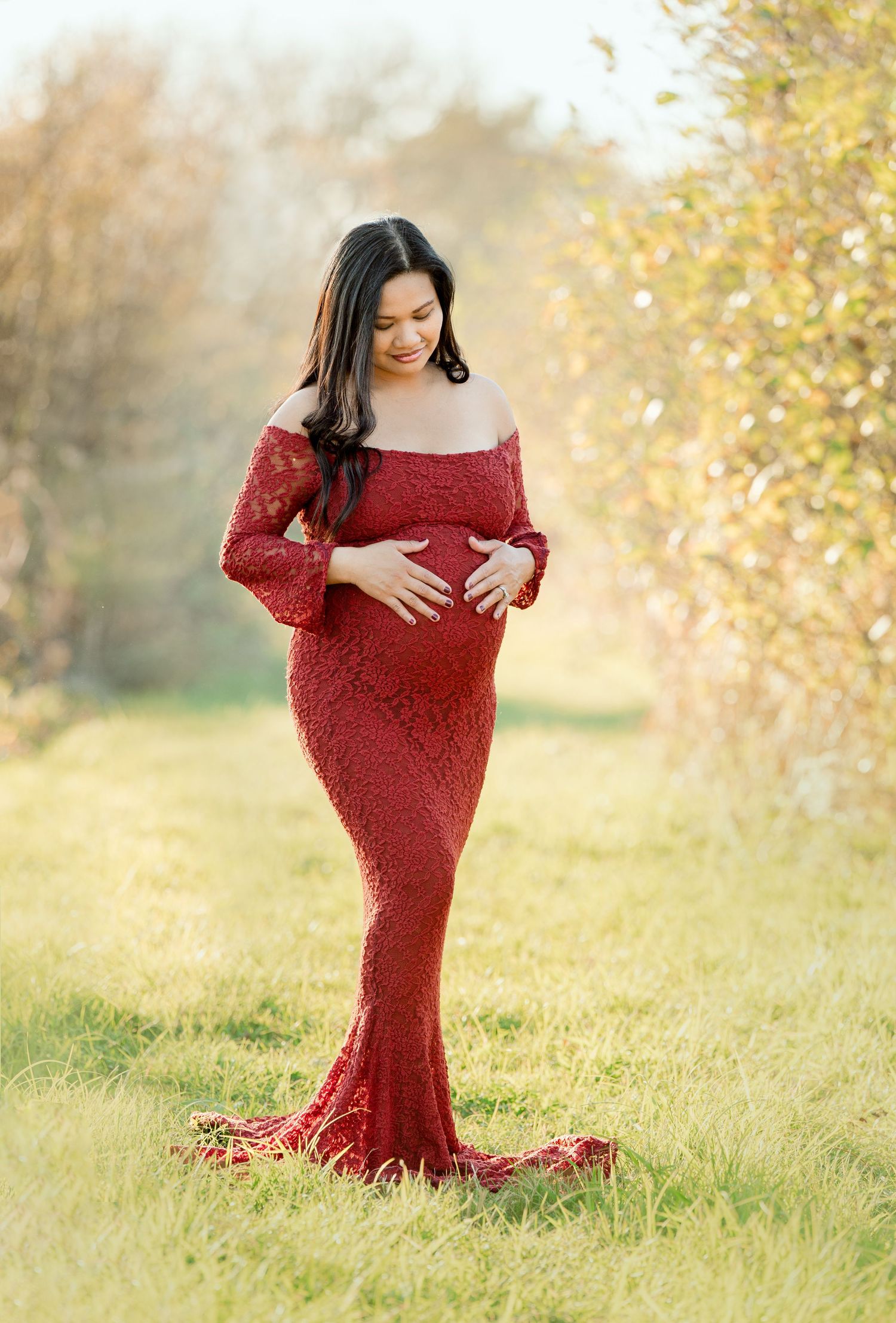Expectant mother in red lace gown poses in golden autumn field.