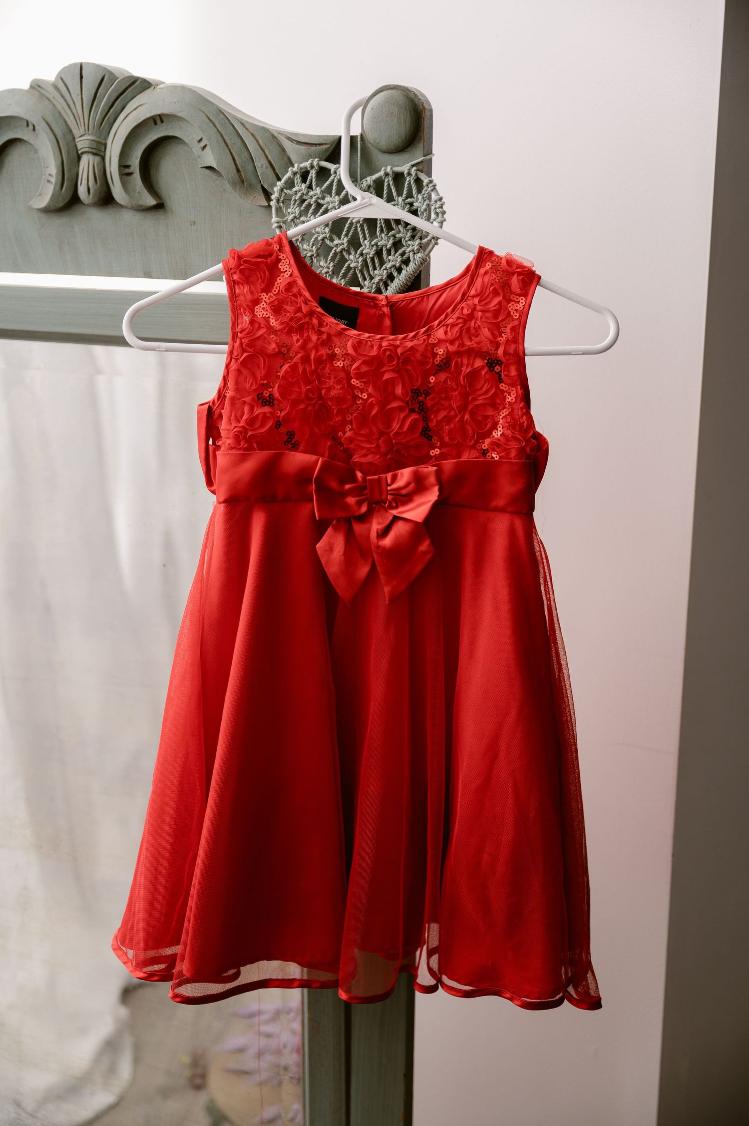 Red formal sleeveless dress with lace bodice and bow detail hanging on gray hanger against white background.